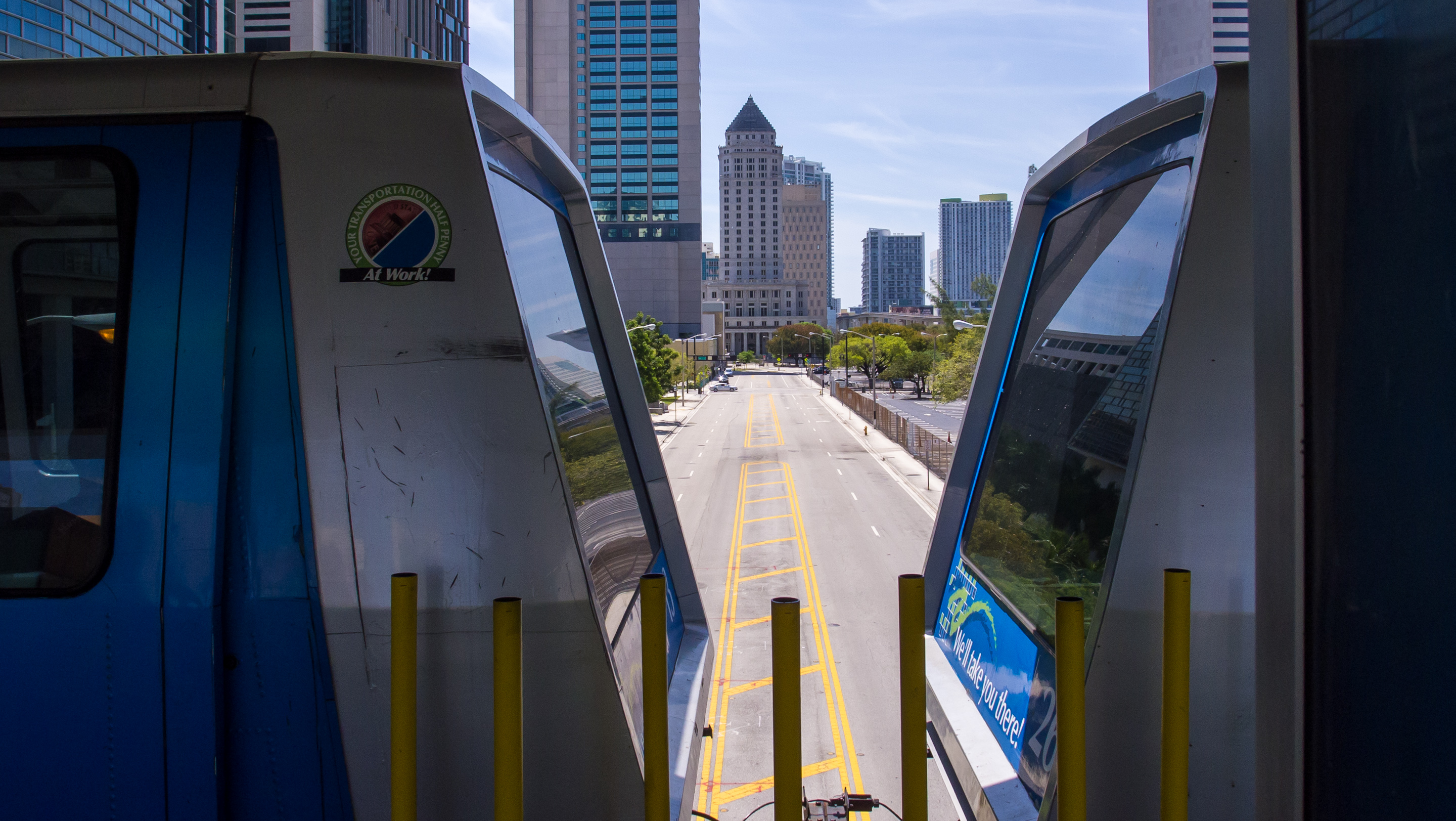 Two Metromover train cars at a station with courthouse and government high-rises visible in the background.