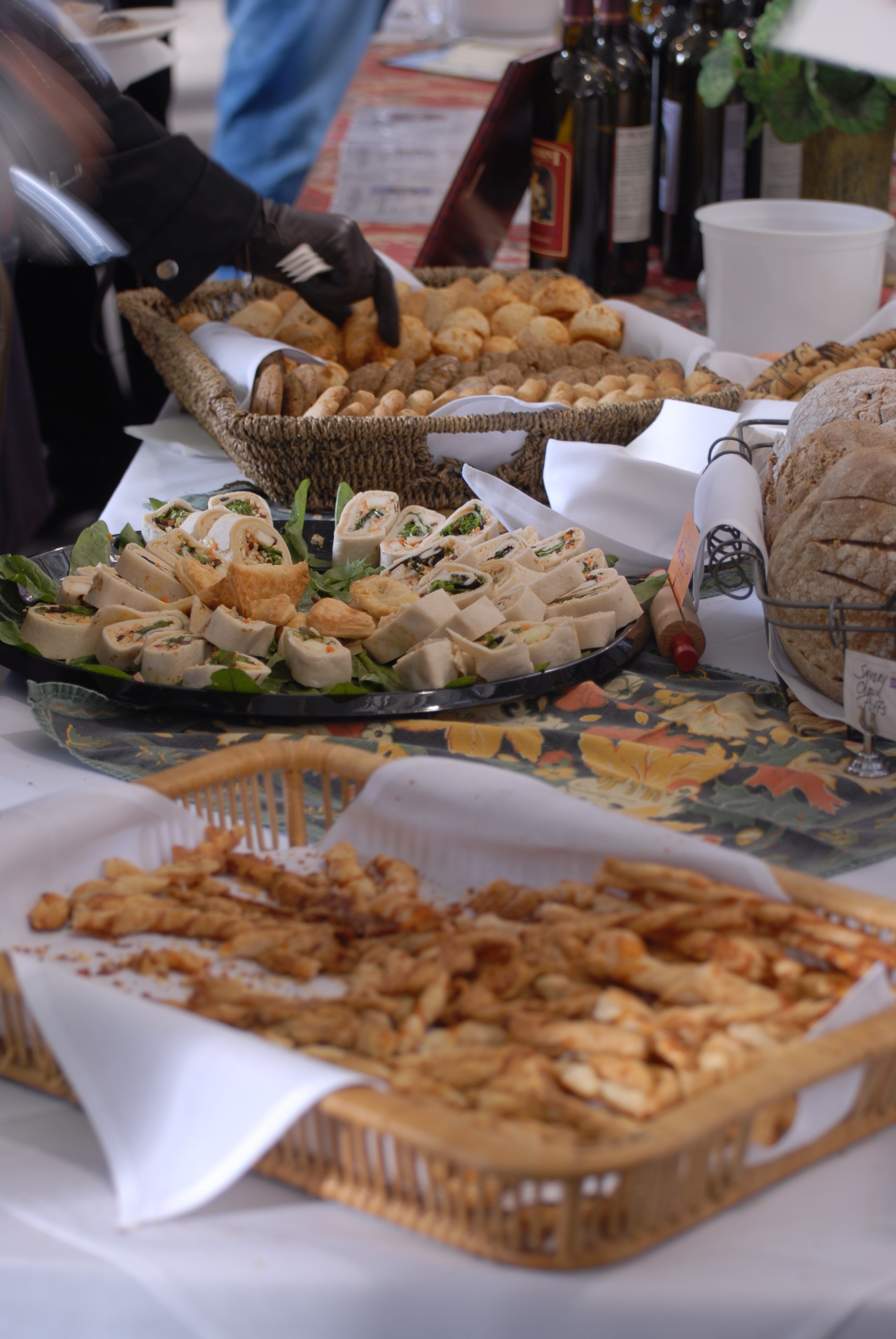 Buffet table with trays of canapés, bread rolls, and wine bottles at a tasting event.