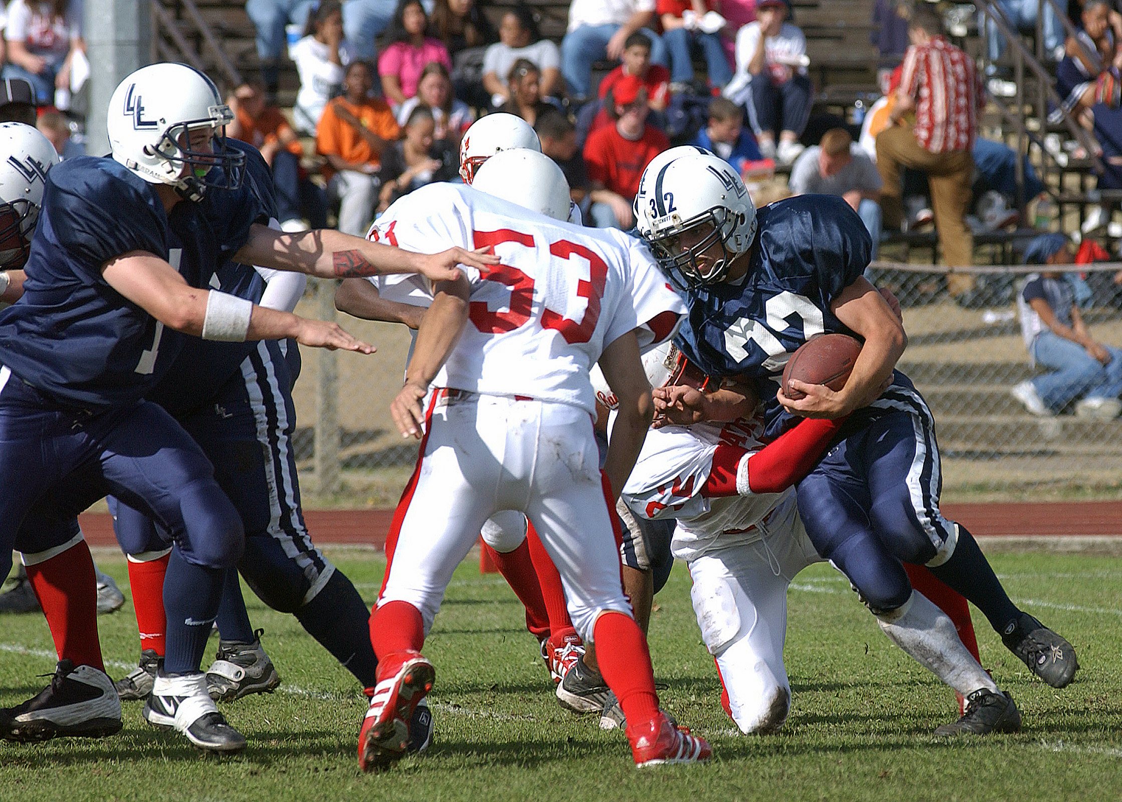 A ball carrier in a navy blue uniform attempts to break through defenders during a high school football game.