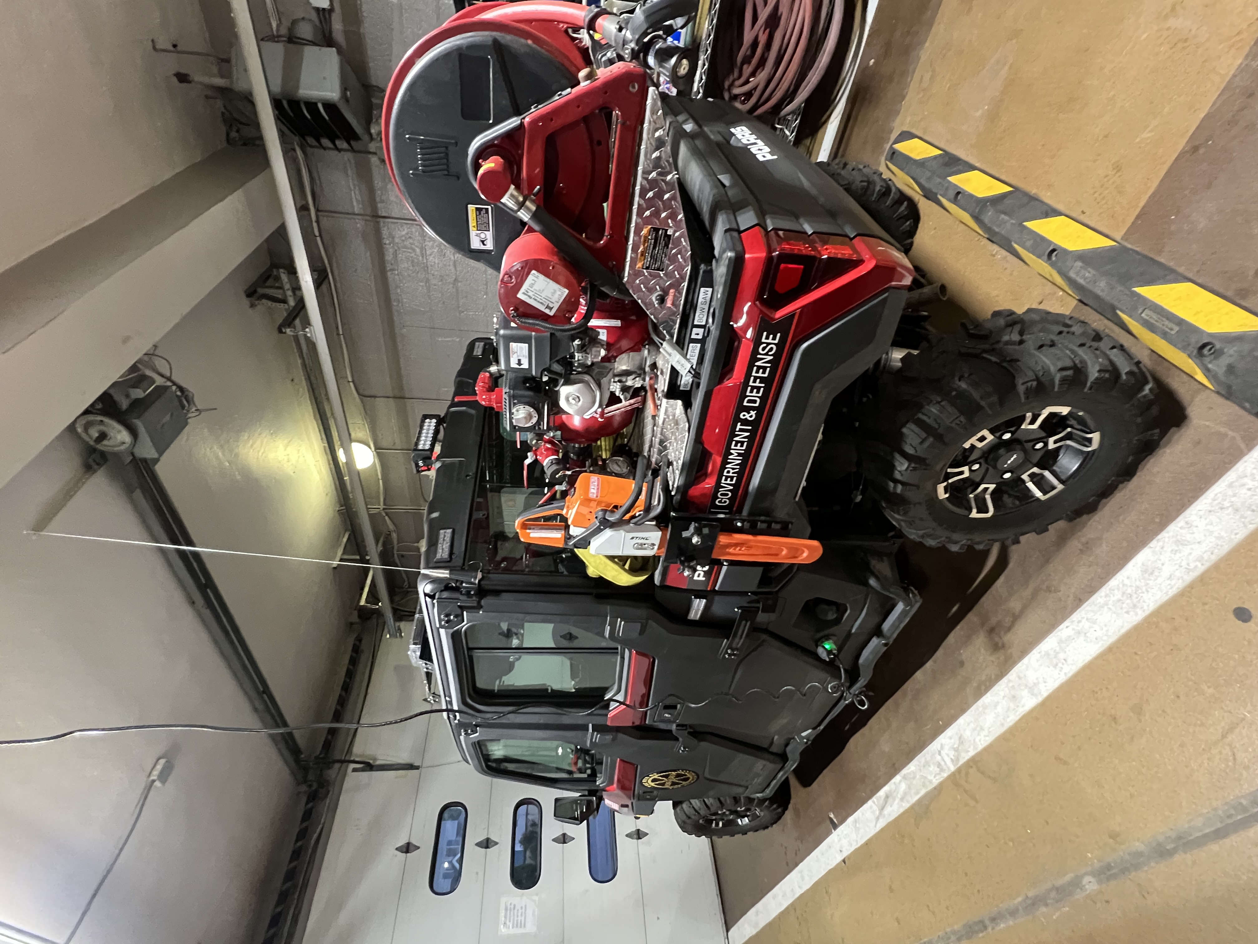 A red and black Polaris Ranger utility vehicle parked inside a garage bay.