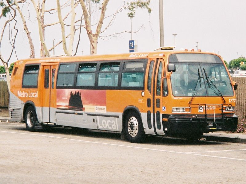 An orange LA Metro Local bus parked in a lot, with Metro Local branding visible on its side.