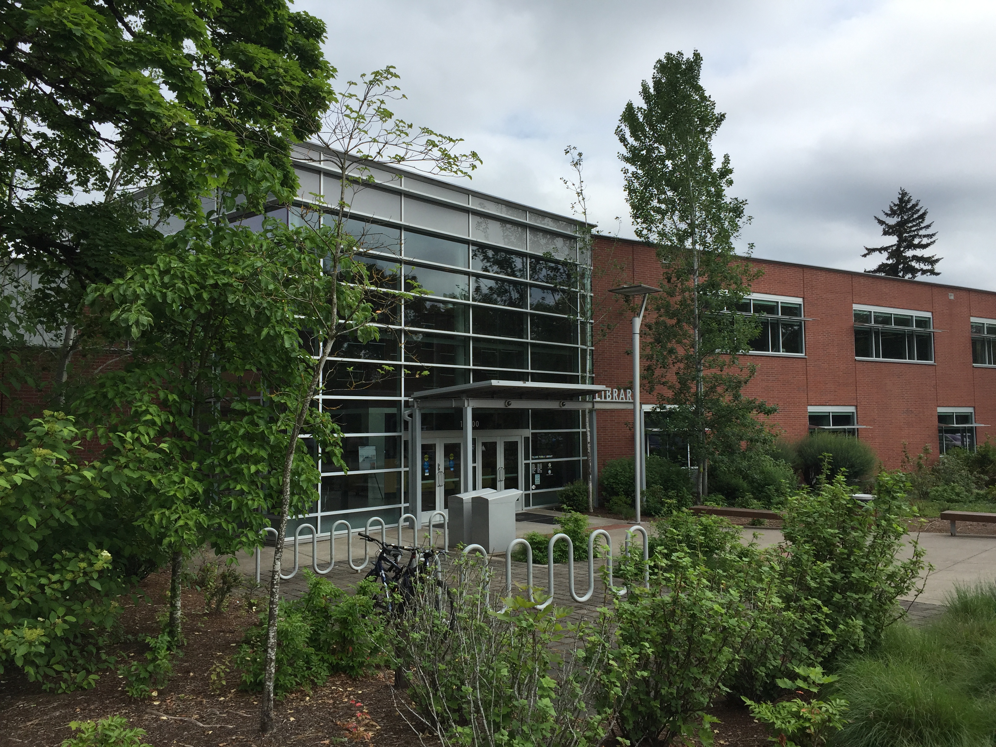 Front entrance of a two-story brick and glass library building with bicycle racks outside.