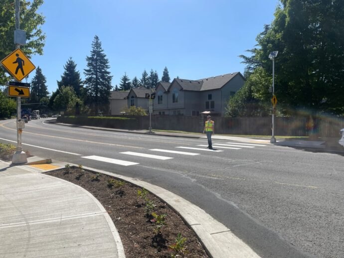 Worker in yellow safety vest standing in a freshly painted crosswalk at a street intersection.