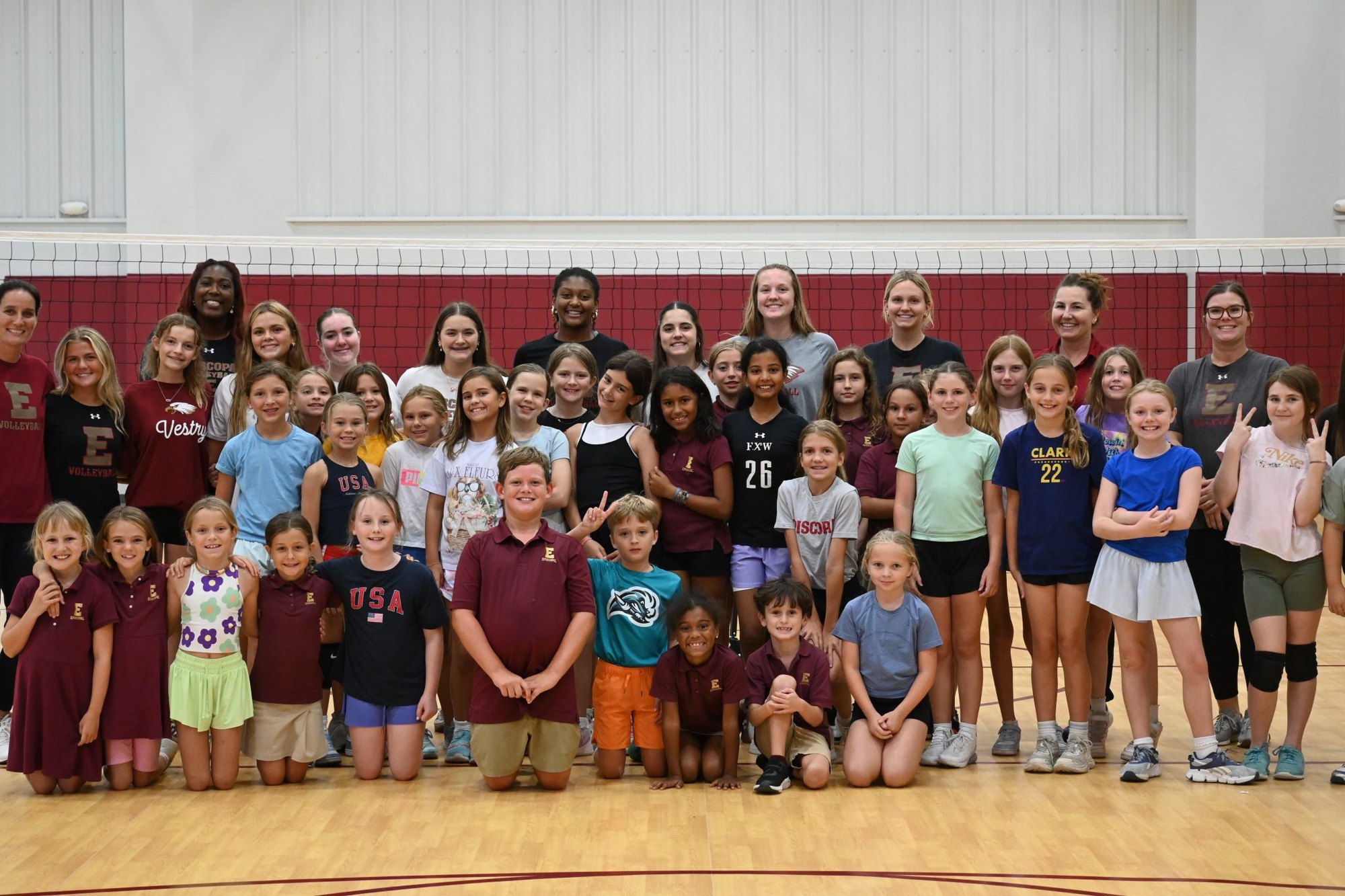 Large group of children and teenagers posing together in a gymnasium with volleyball nets.
