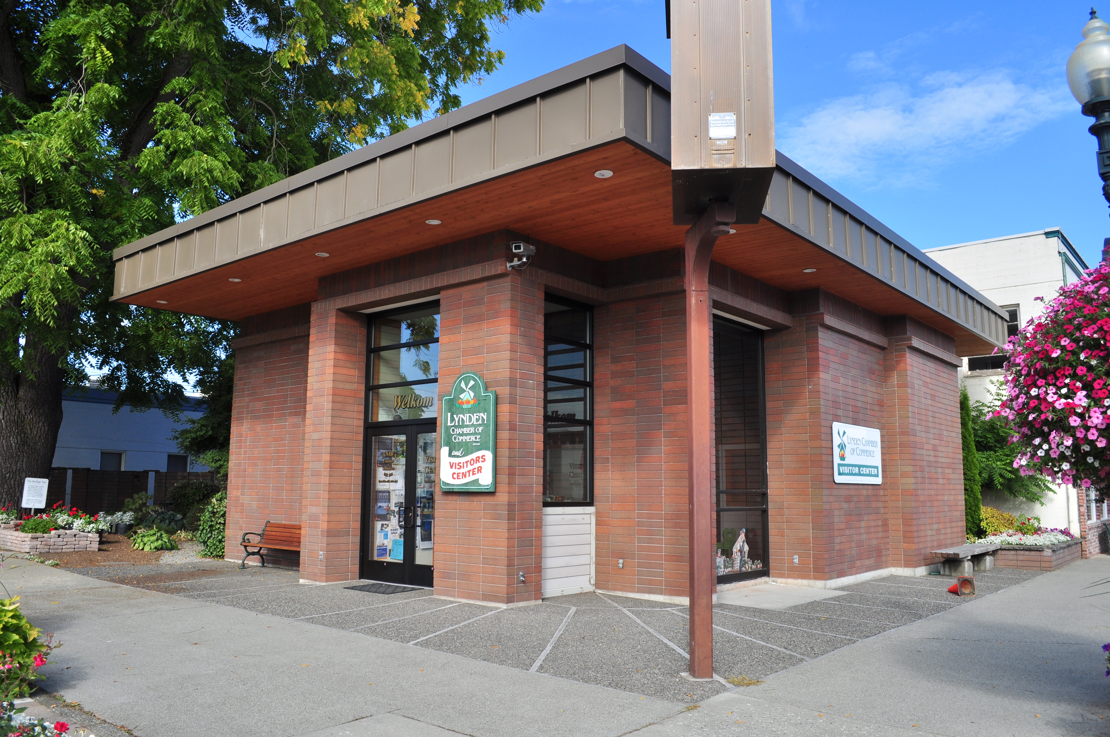 Single-story brick chamber of commerce building with hanging flower baskets and glass entrance doors.