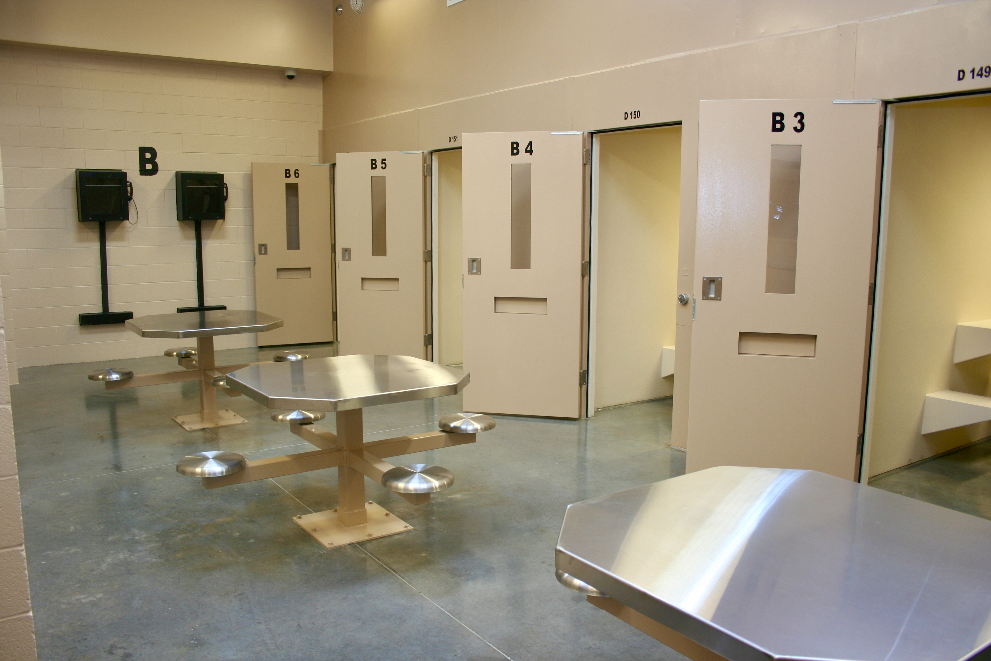 Interior of a jail housing unit with numbered cell doors and bolted-down steel tables.