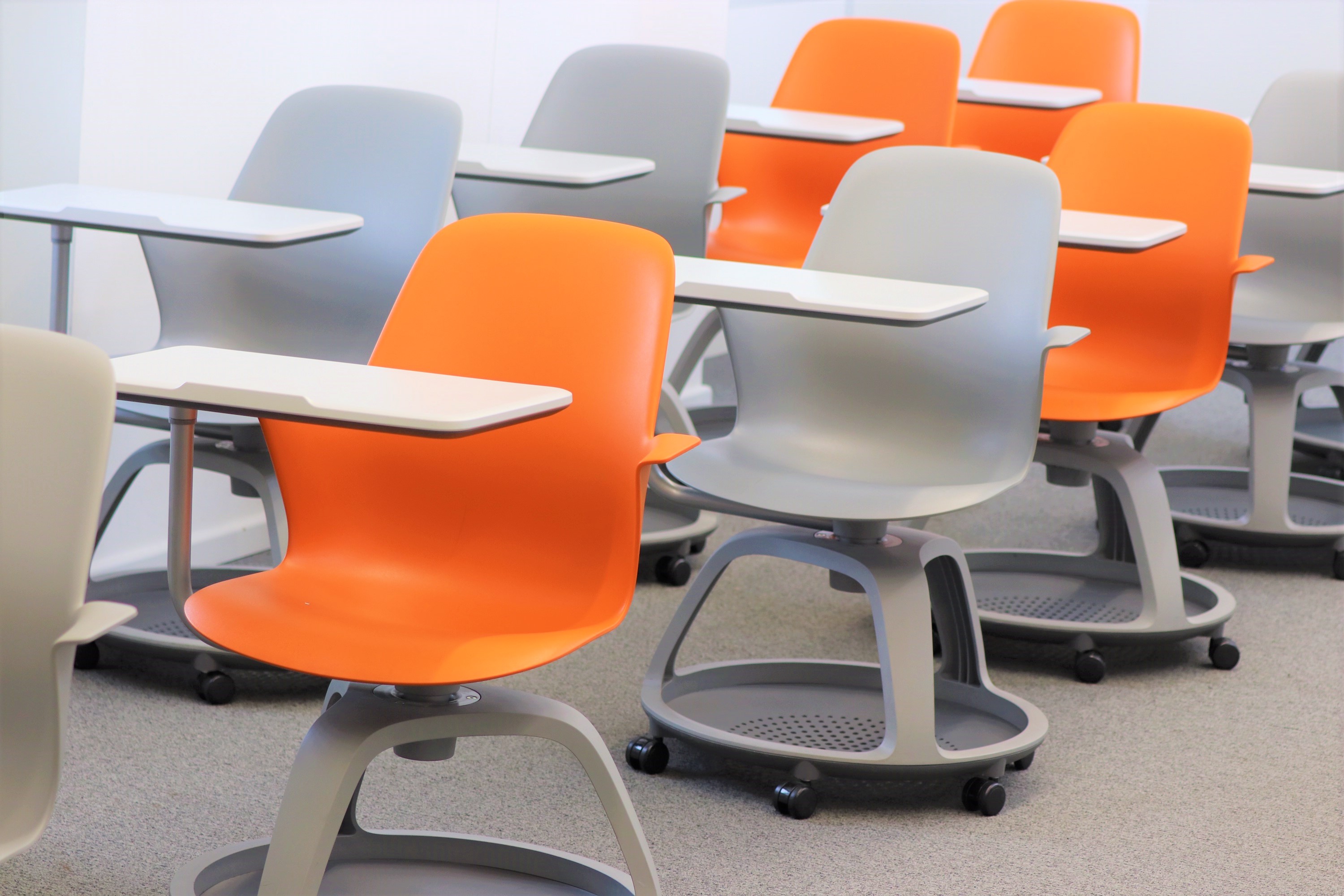 Rows of modern orange and gray student chairs with writing tablets in an empty classroom.