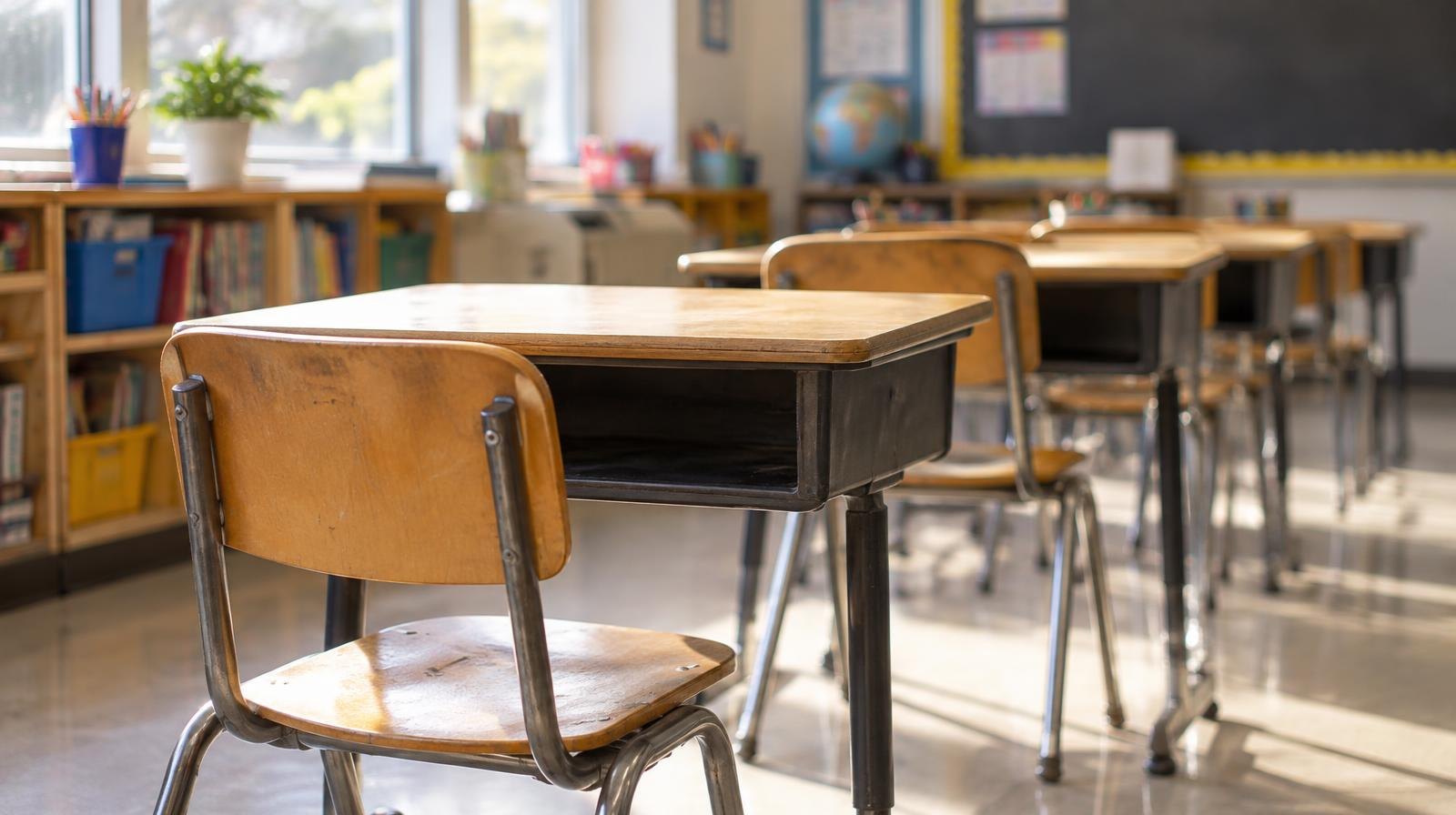 Rows of small wooden student desks and chairs sitting empty in a sunlit classroom.