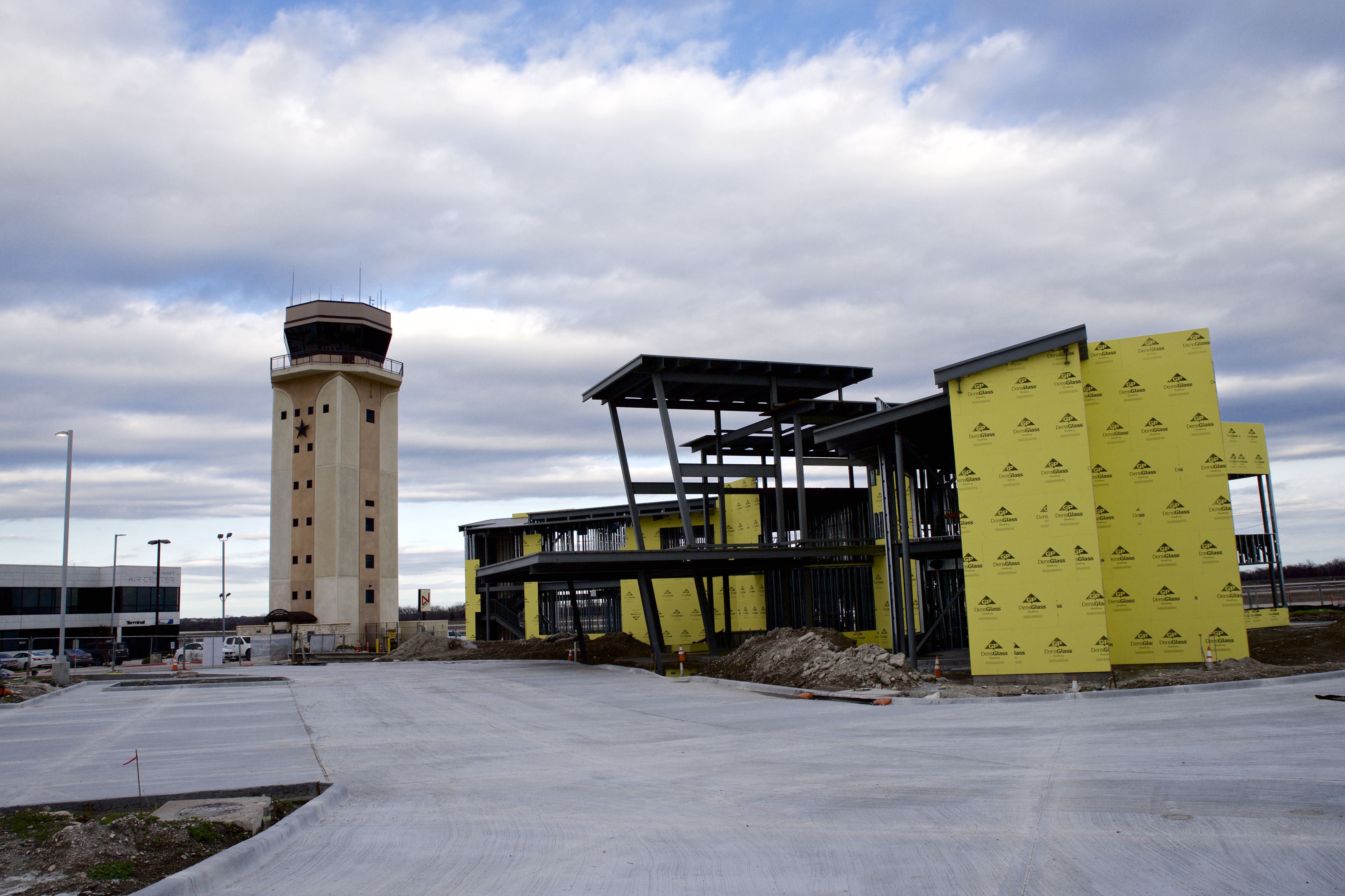 Airport control tower next to a partially constructed terminal building wrapped in yellow sheeting.