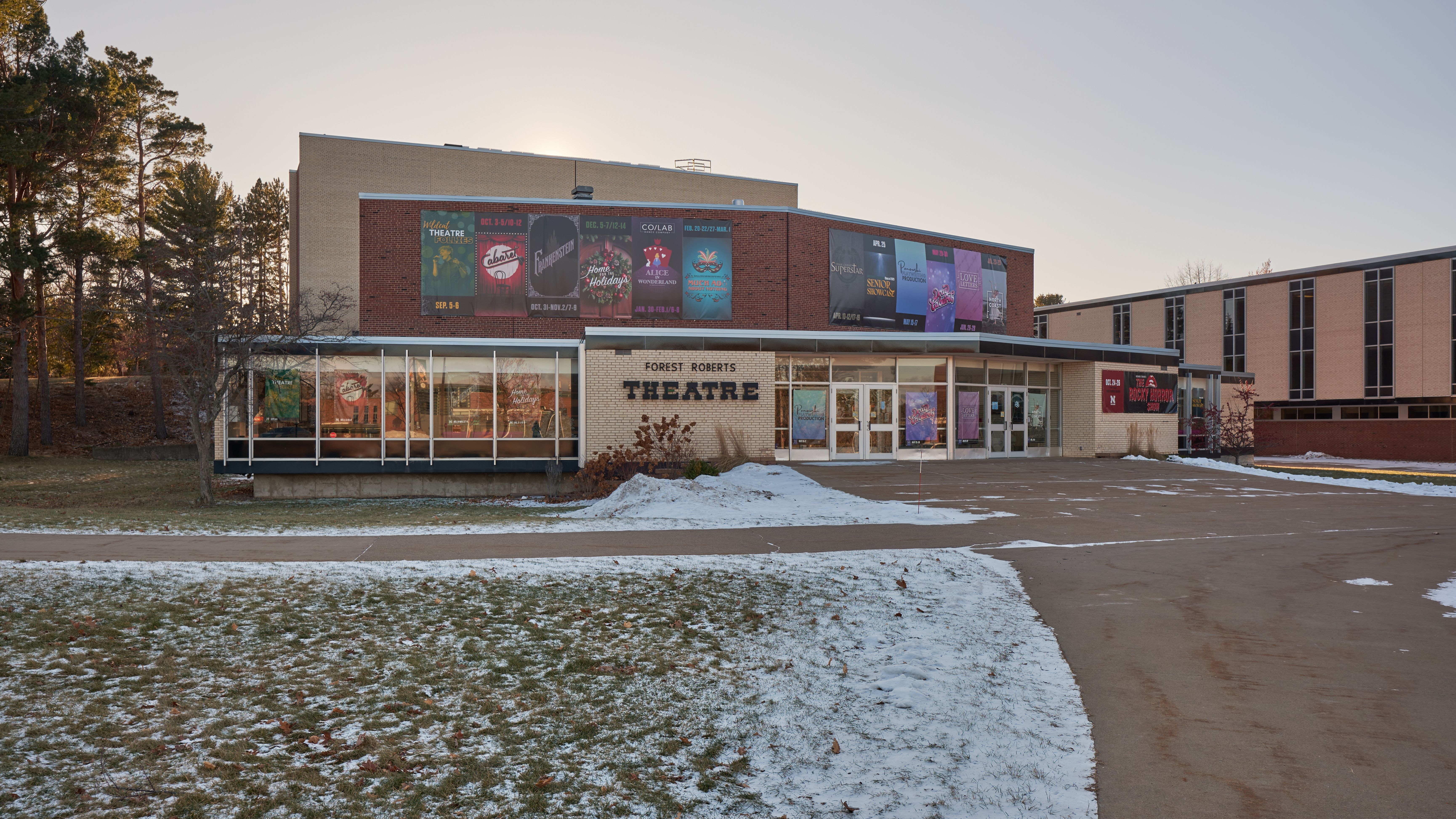 Glass-fronted entrance of a brick theater building with light snow on the ground.