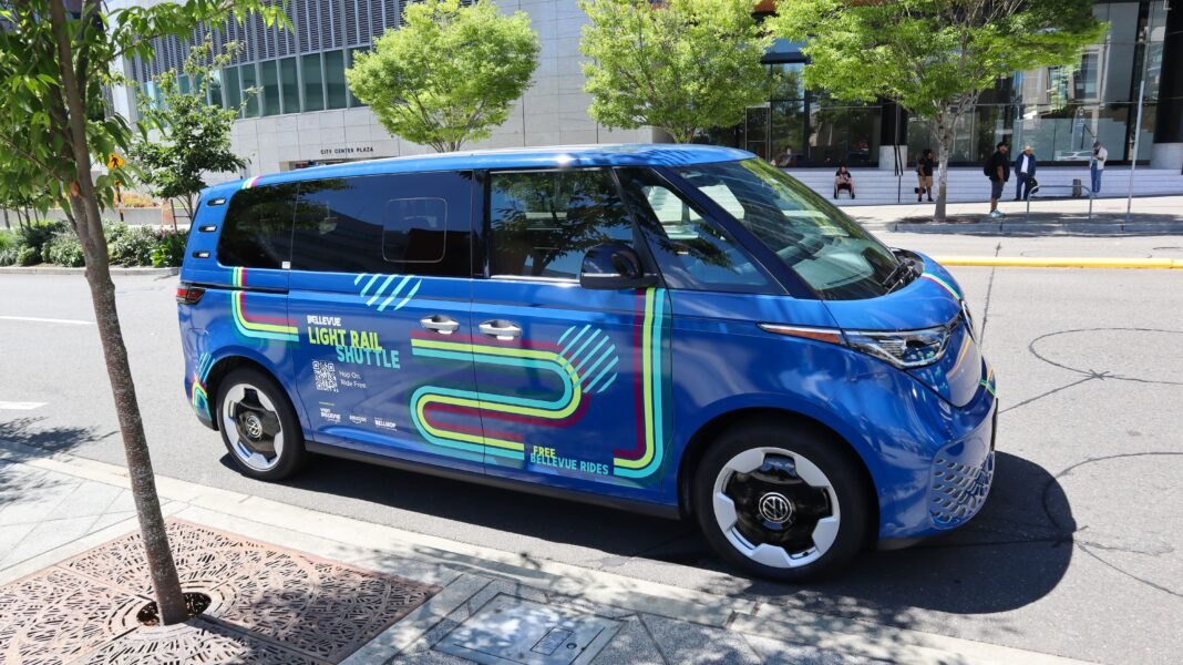 Blue electric van with colorful Light Rail Shuttle branding parked on a city street.