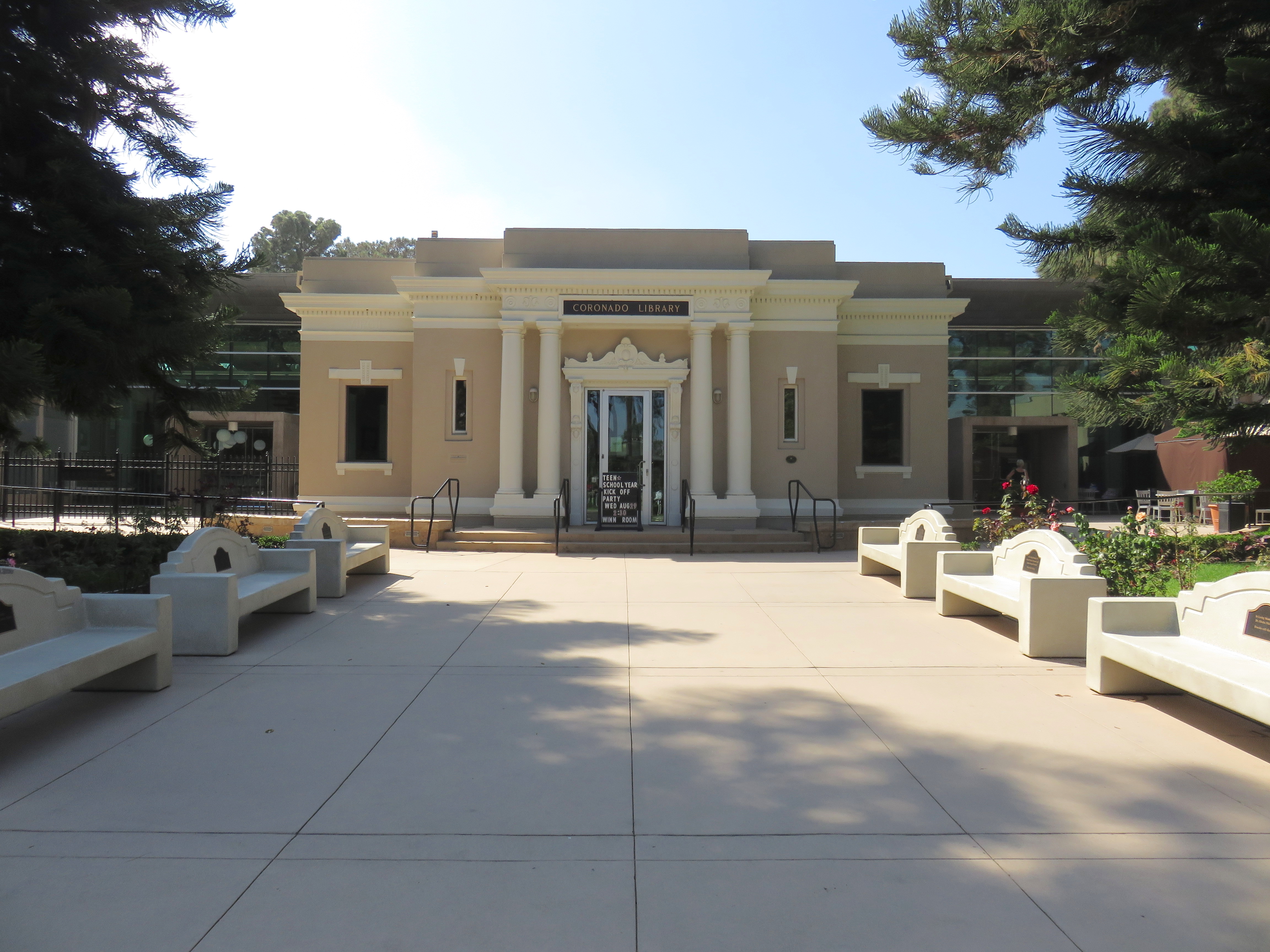 Exterior of a neoclassical library building with white columns and a paved plaza in front.