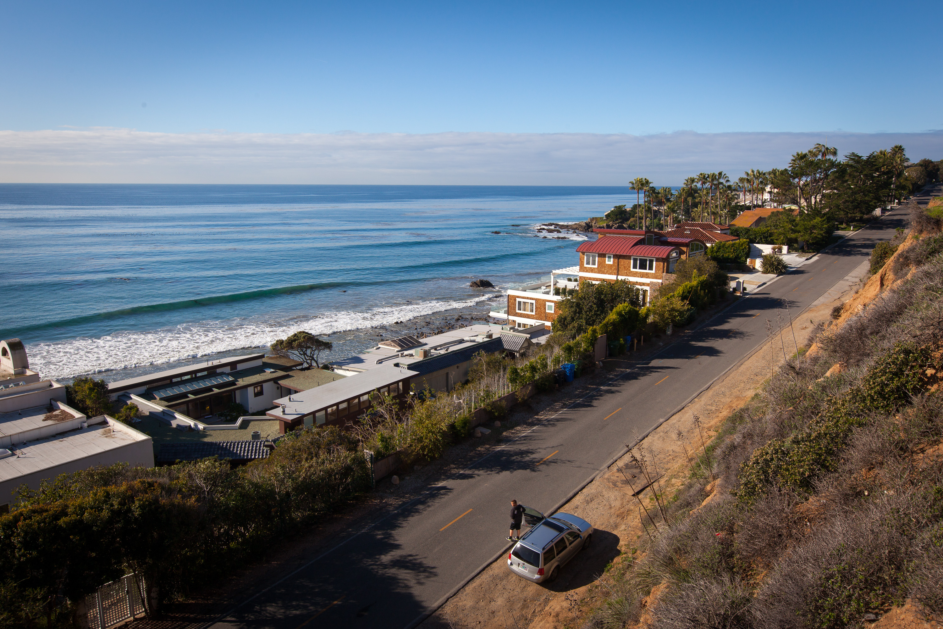 Aerial view of a coastal road running alongside the Pacific Ocean with breaking waves.