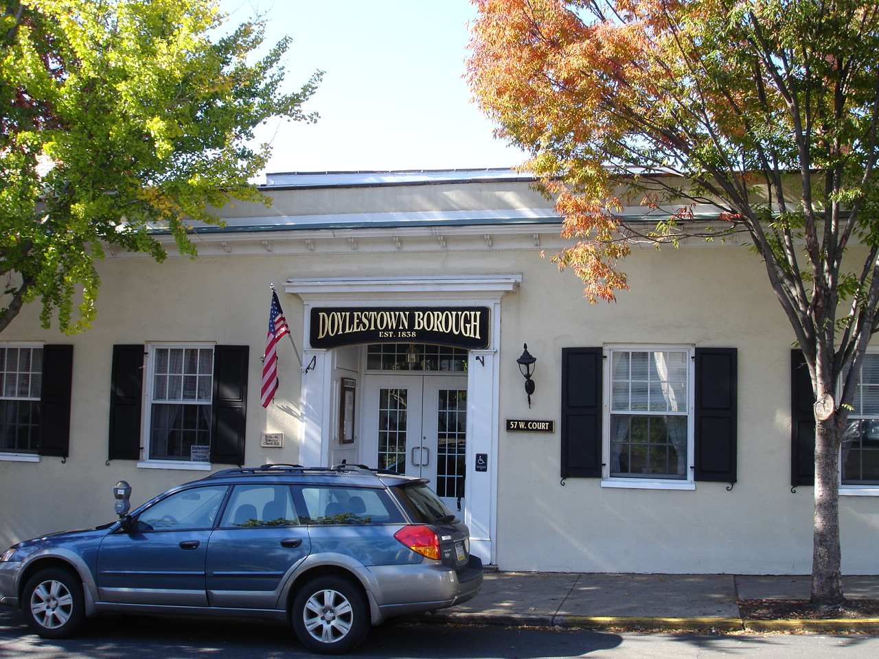 White stucco borough hall building with black shutters and American flag at entrance