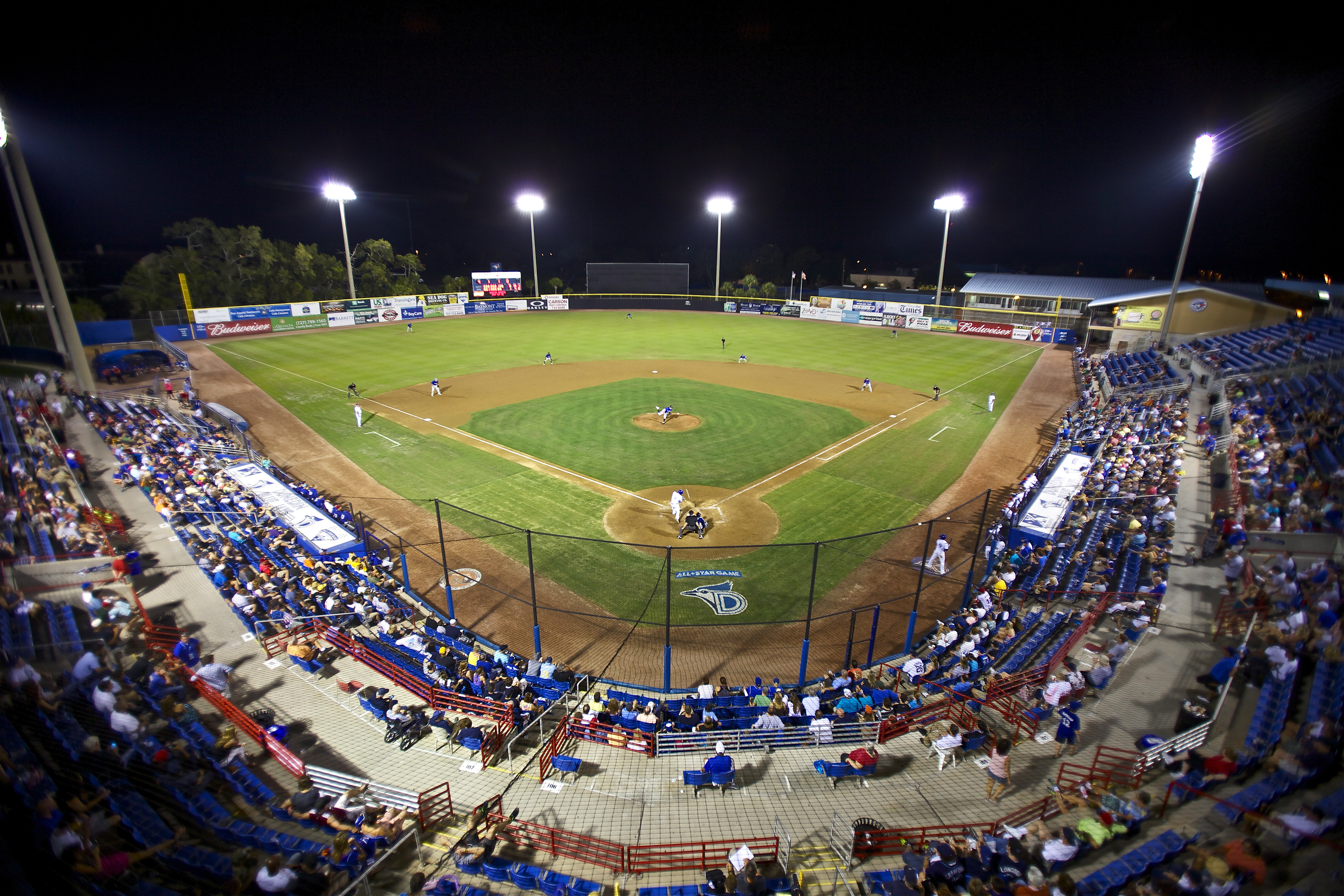 Aerial night view of a lit baseball stadium filled with spectators.