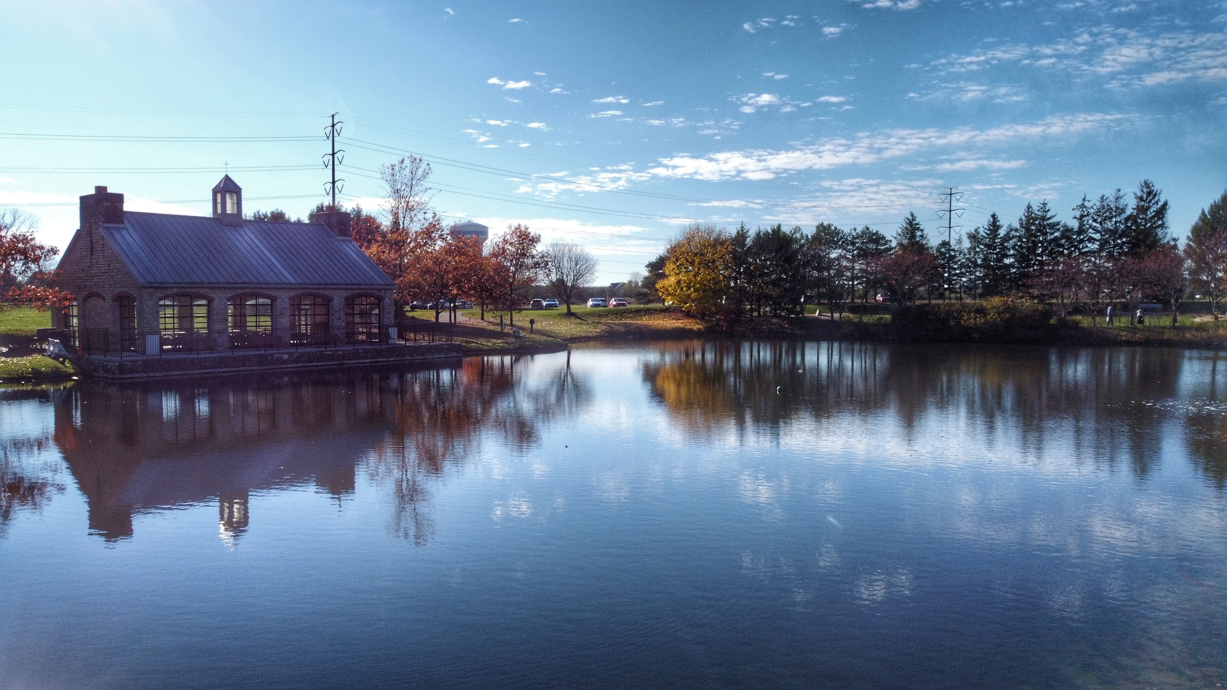 Reflective pond with stone pavilion and autumn-colored trees at a public park.