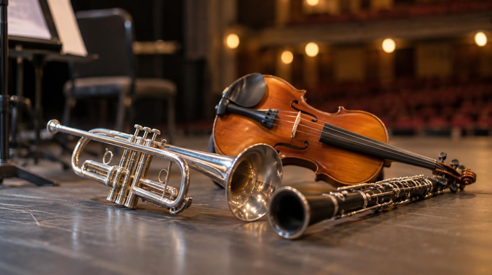 A silver trumpet, wooden violin, and black clarinet arranged together under stage spotlights.