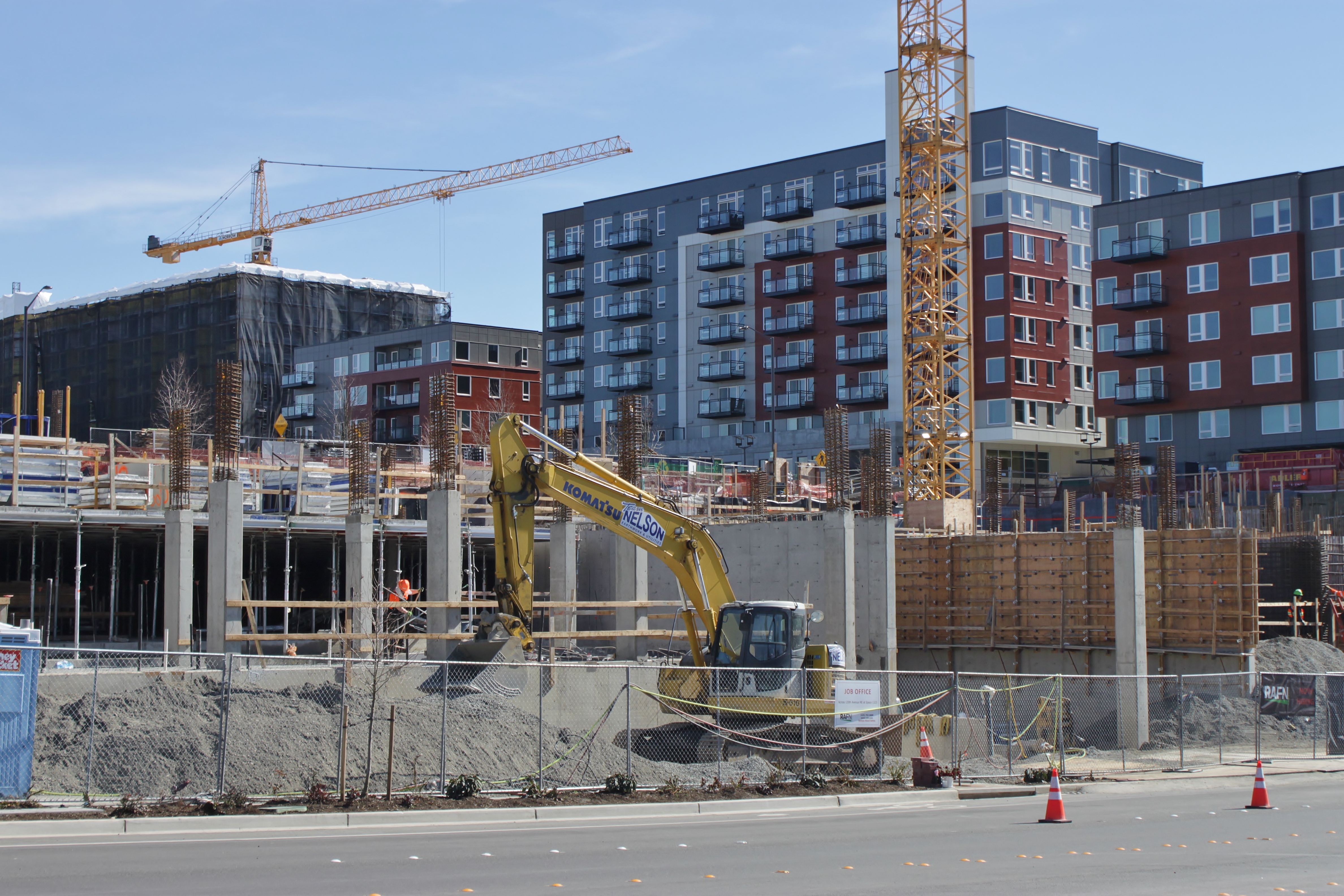 Yellow excavator and tower cranes at an active apartment construction site in Bellevue.