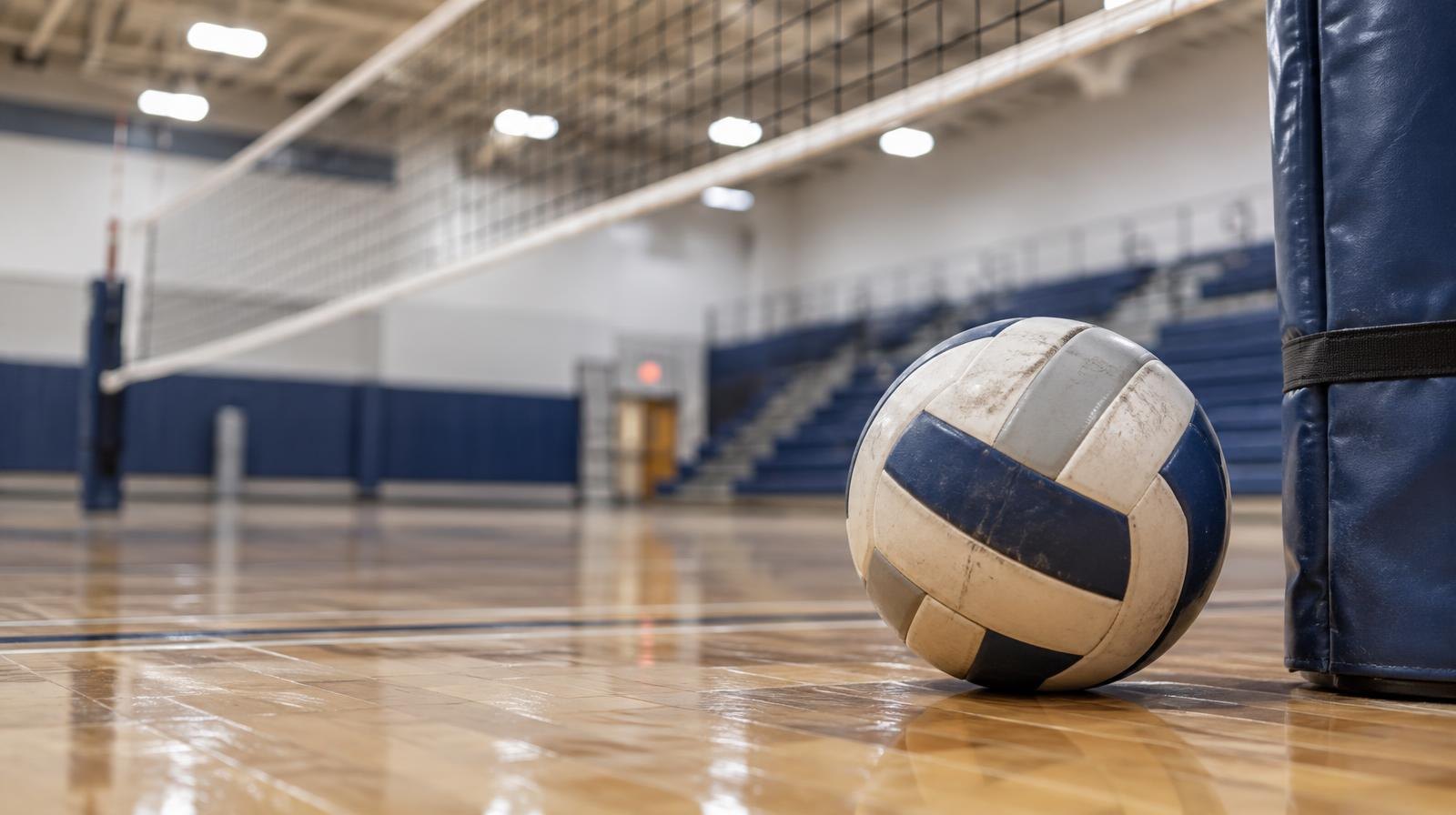 A volleyball resting on a hardwood gymnasium floor beside a net post.