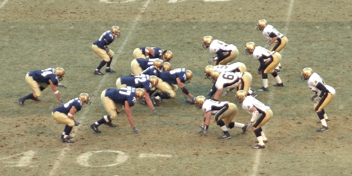 Football players from two teams crouched at the line of scrimmage before the snap.