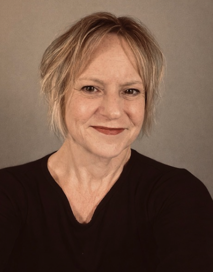 Jackie Coleman smiles, wearing a black top against a beige background.