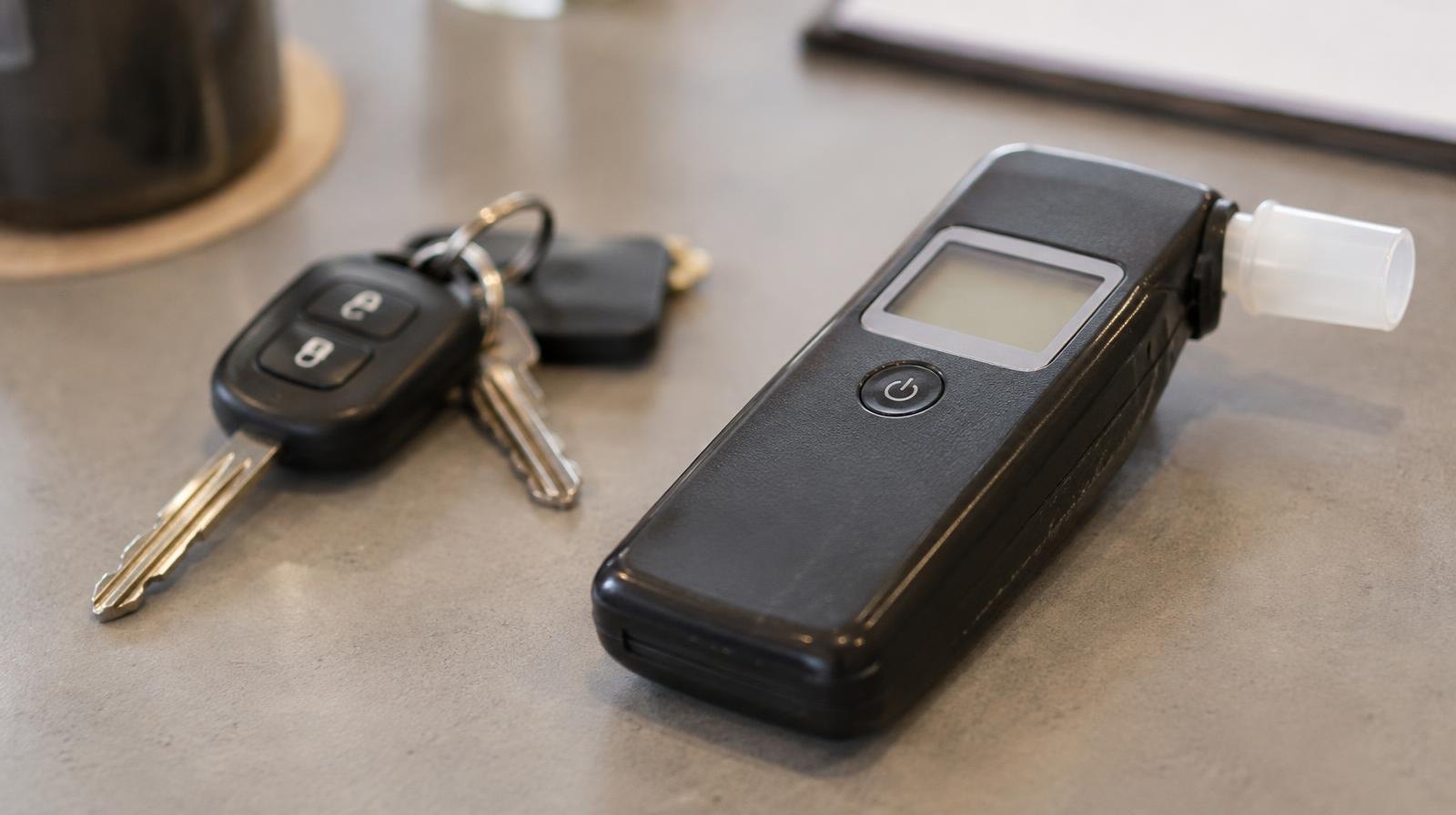 A breathalyzer device resting beside a set of car keys on a flat surface.