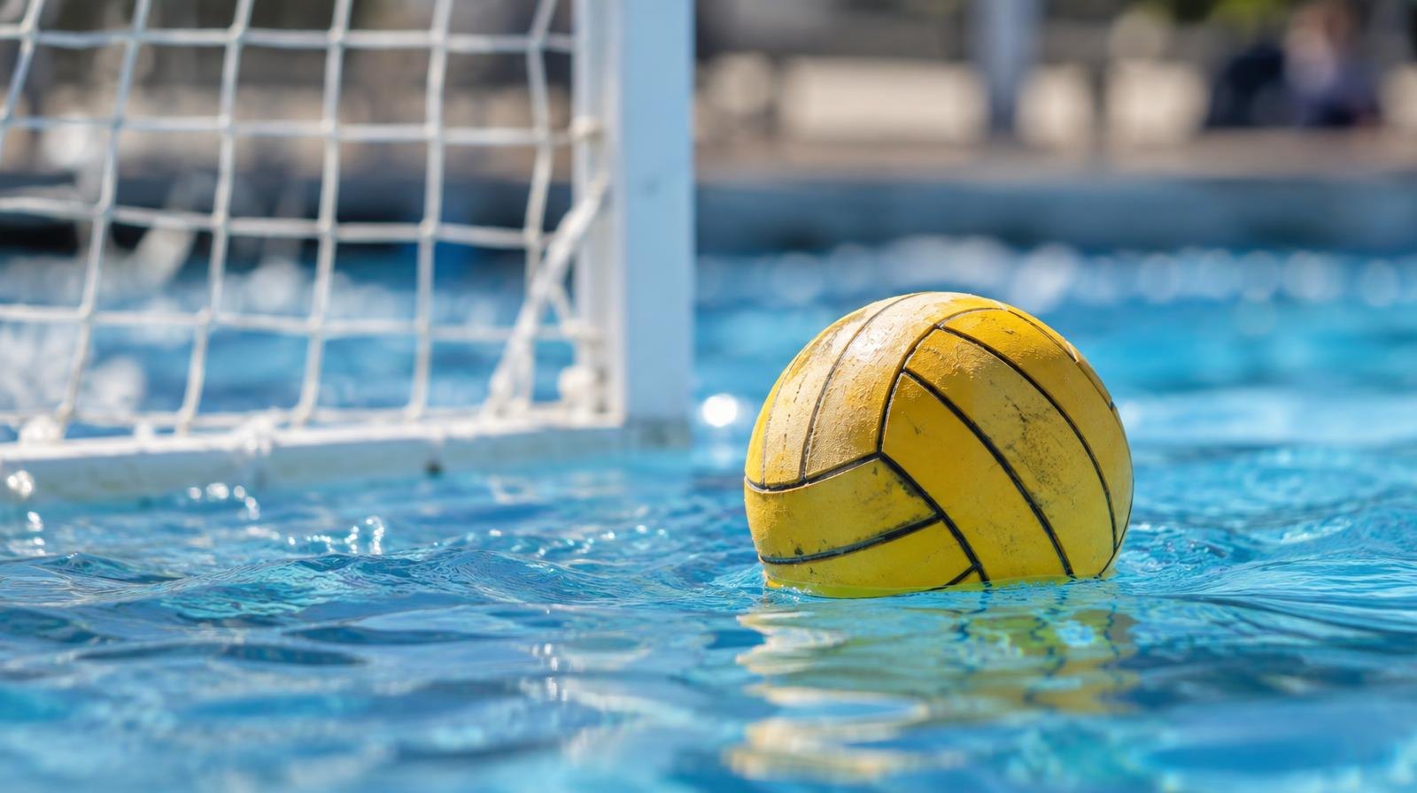 A water polo ball floating on the surface of a bright blue pool near a white goal net.