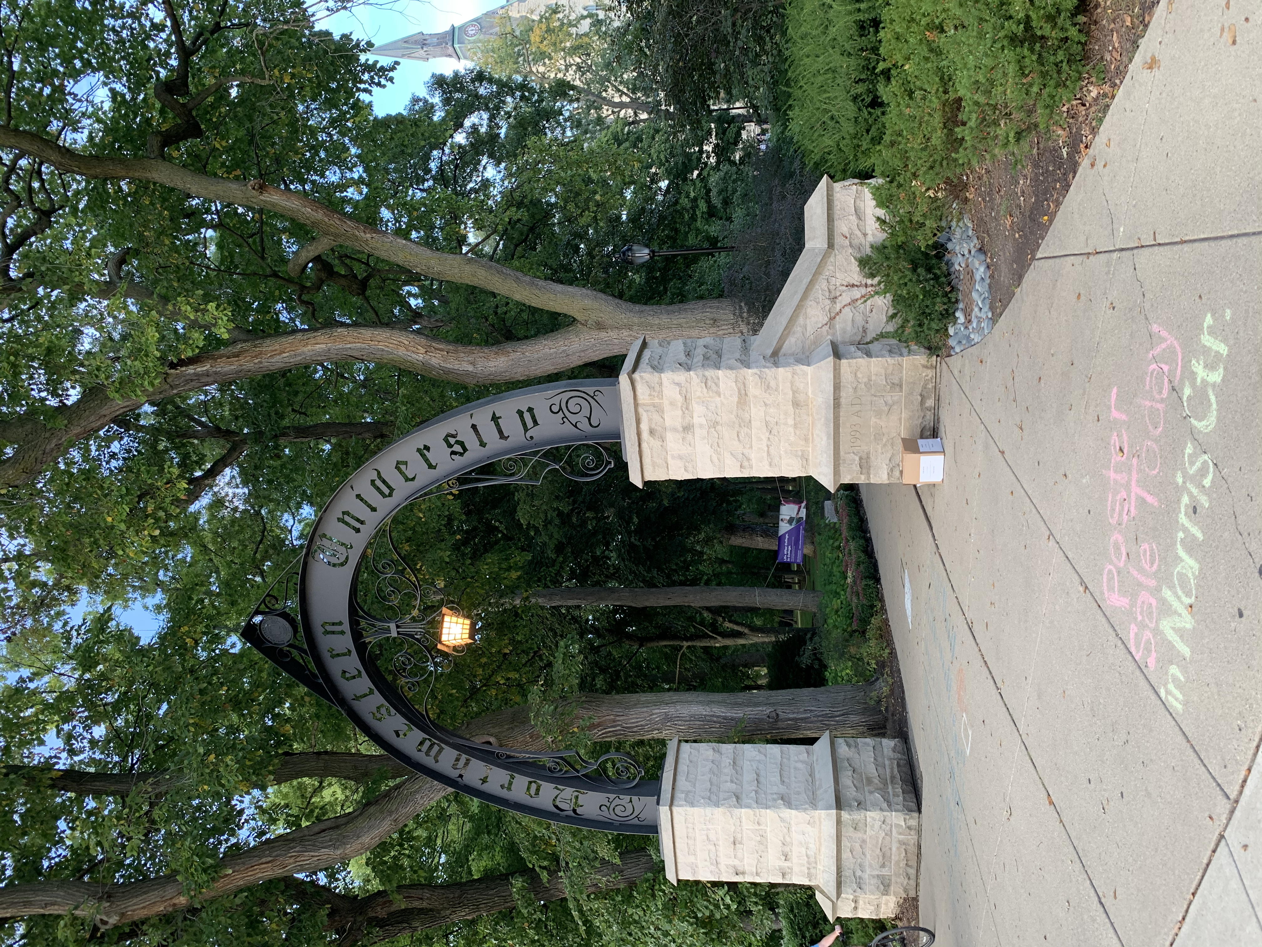 Northwestern University iron arch gateway with stone pillars surrounded by mature trees on campus.