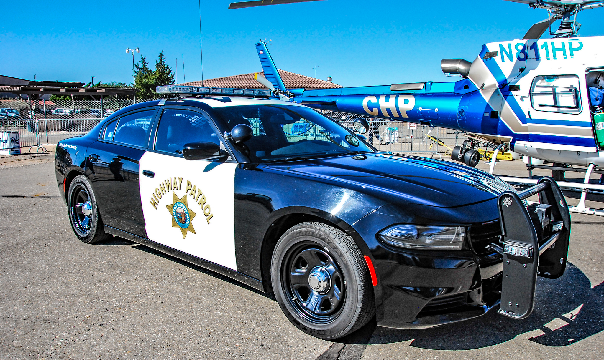 Black-and-white California Highway Patrol Dodge Charger patrol car with a CHP helicopter visible behind it.