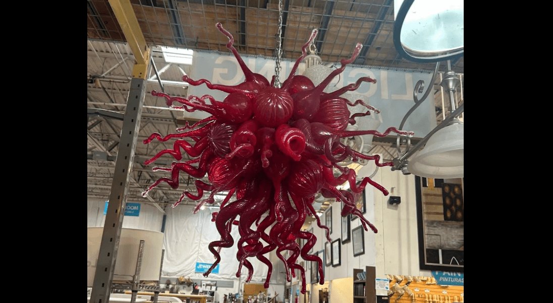 A deep red blown-glass sculpture with curling tentacle-like extensions hanging from a ceiling.