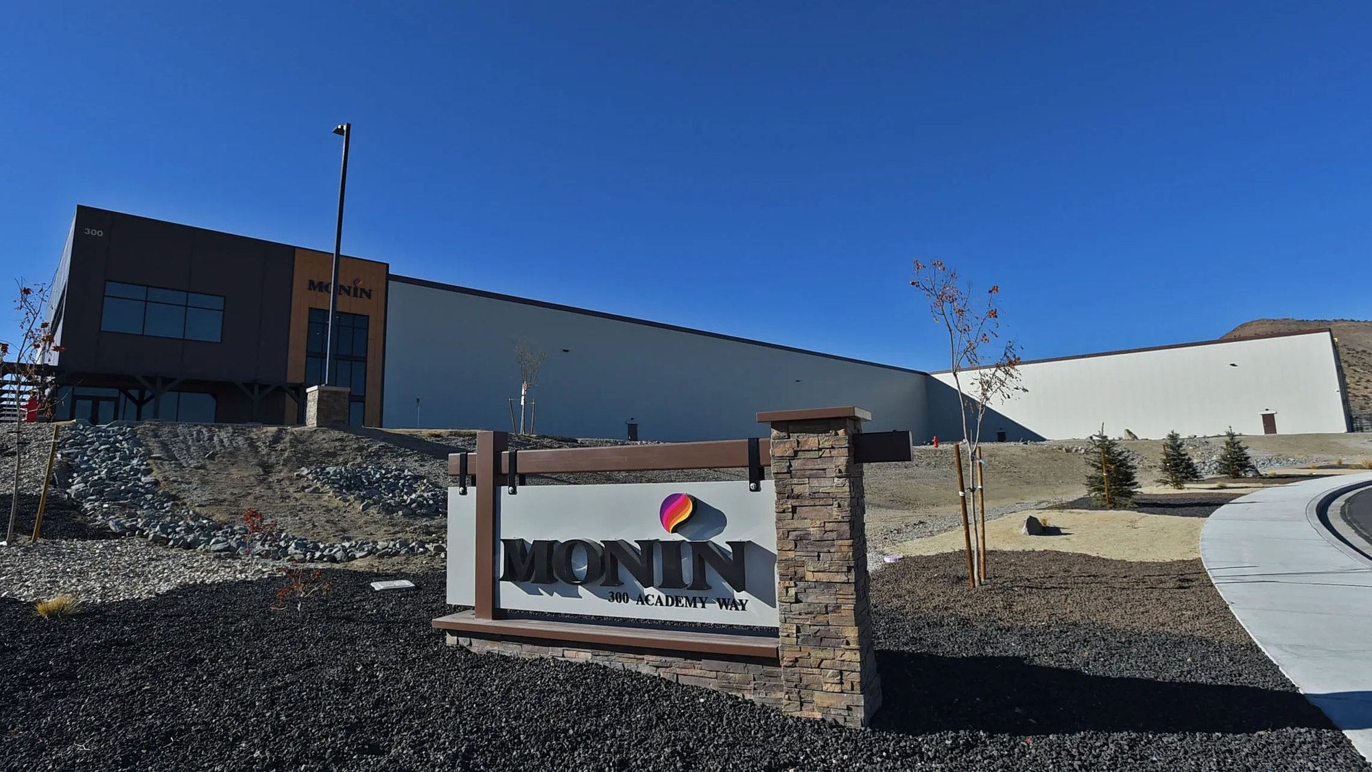 Monument sign reading 'Monin' in front of a large industrial warehouse building.