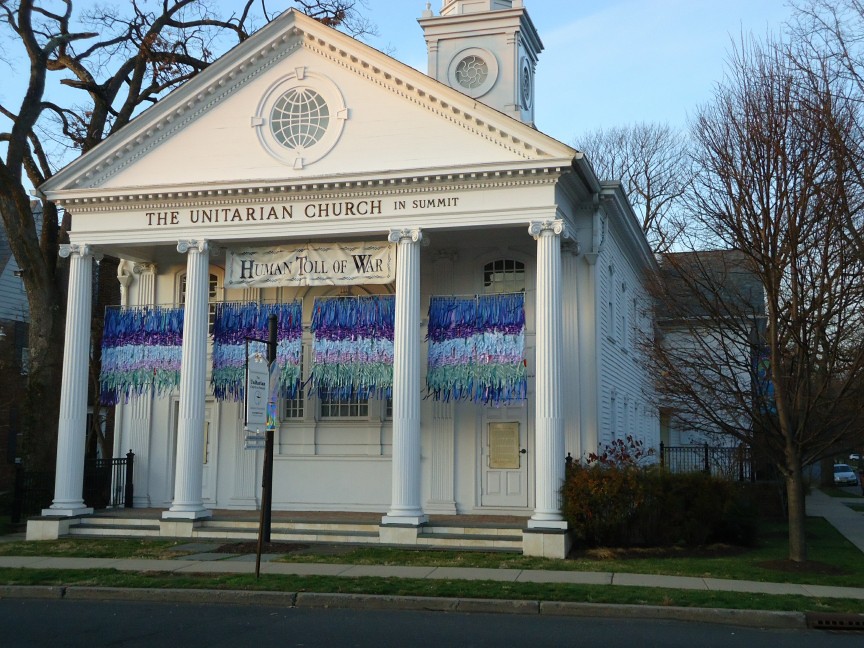 A white clapboard church with classical columns and a bell tower on a tree-lined street.