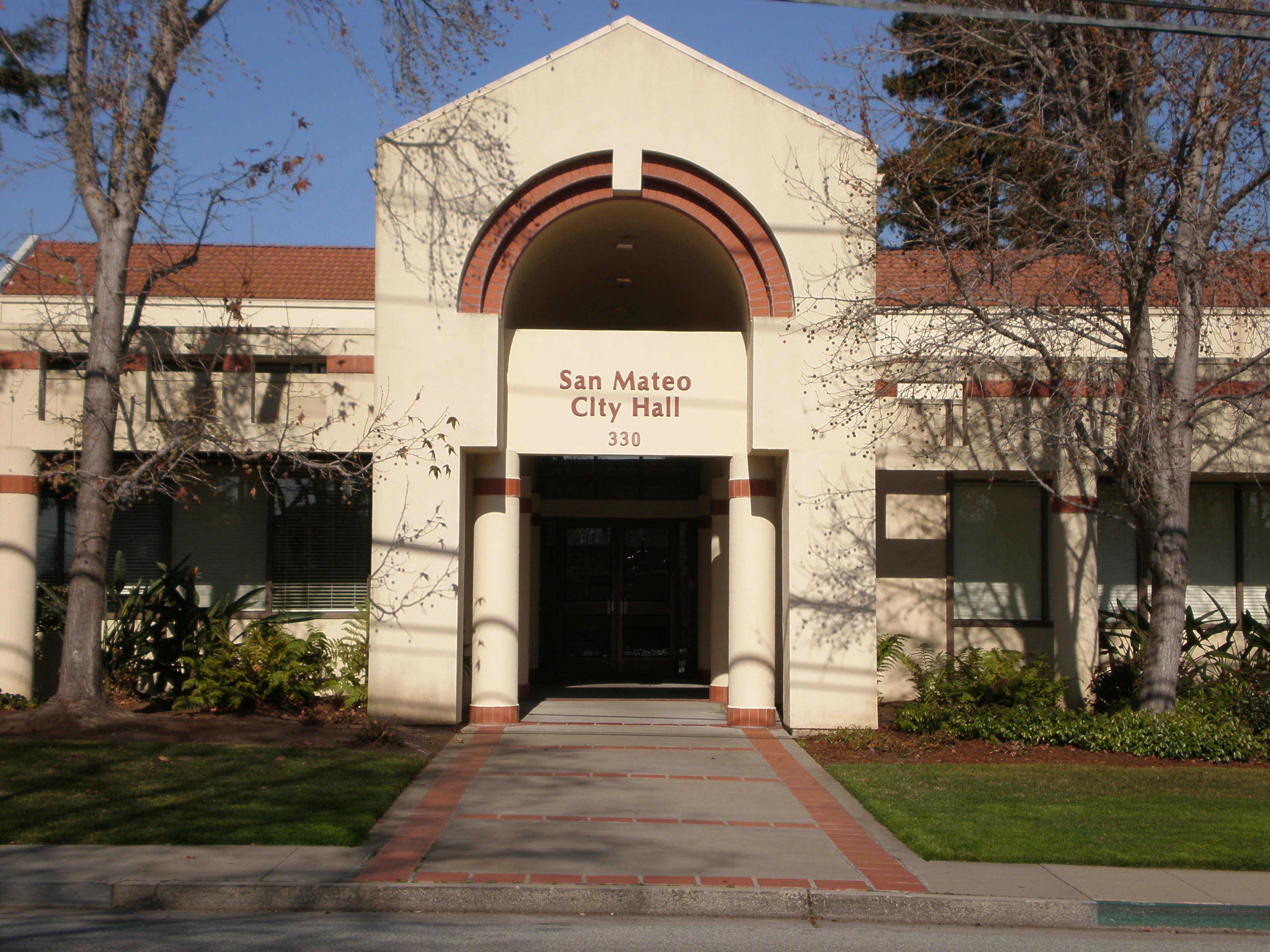 Front entrance of San Mateo City Hall, a modern building with glass doors and an overhang.