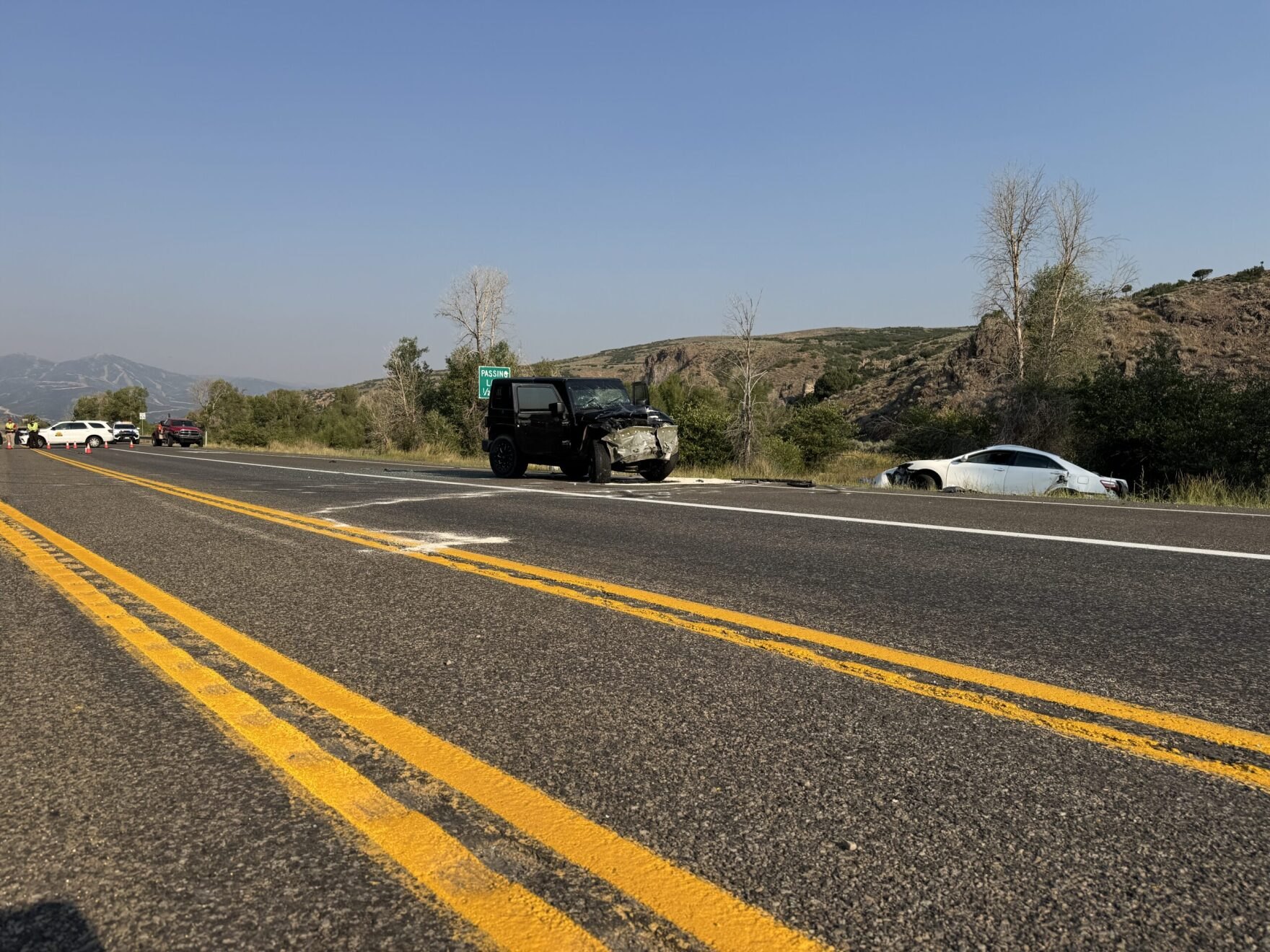 Damaged Jeep Wrangler and white sedan stopped on a two-lane rural highway.