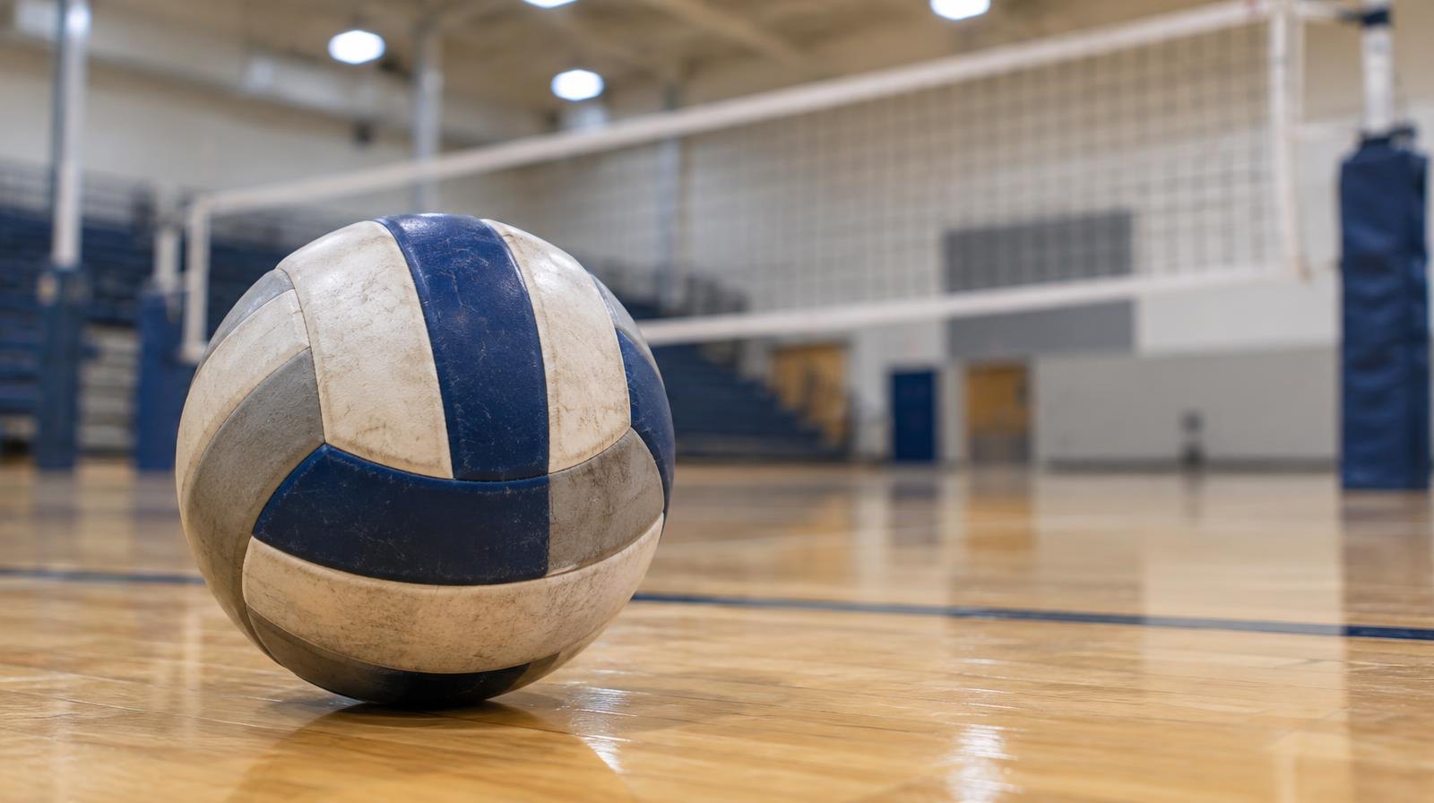 A volleyball resting on a hardwood gymnasium floor near a net.