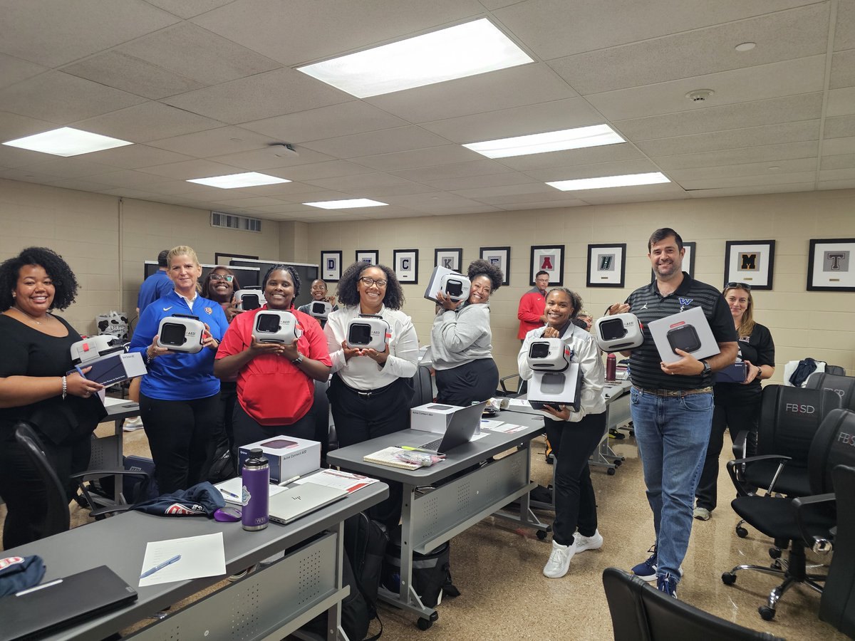 Group of people smiling and holding boxed electronic devices in a training room.