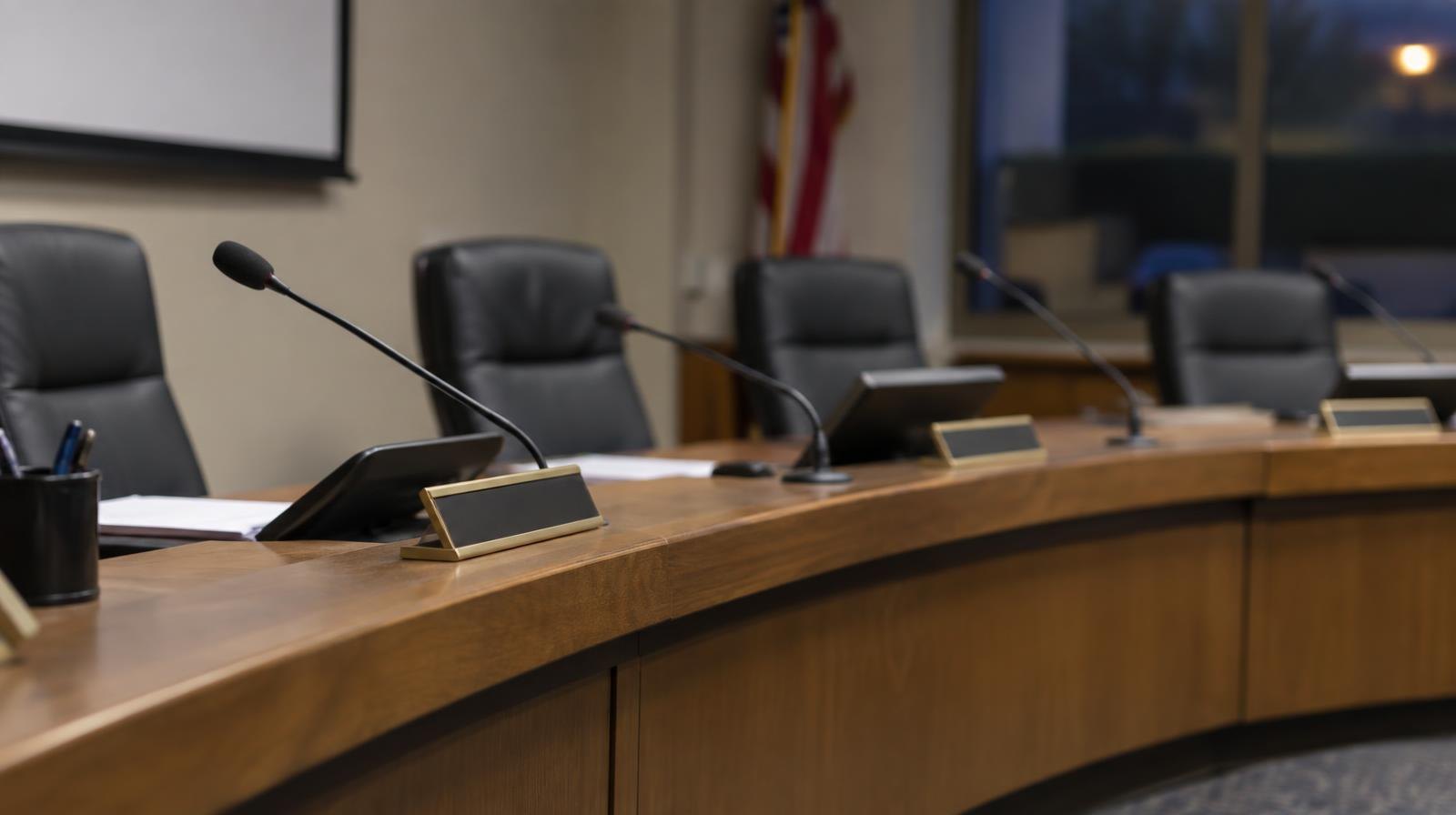 Empty curved dais with microphones and name placards in a meeting room.