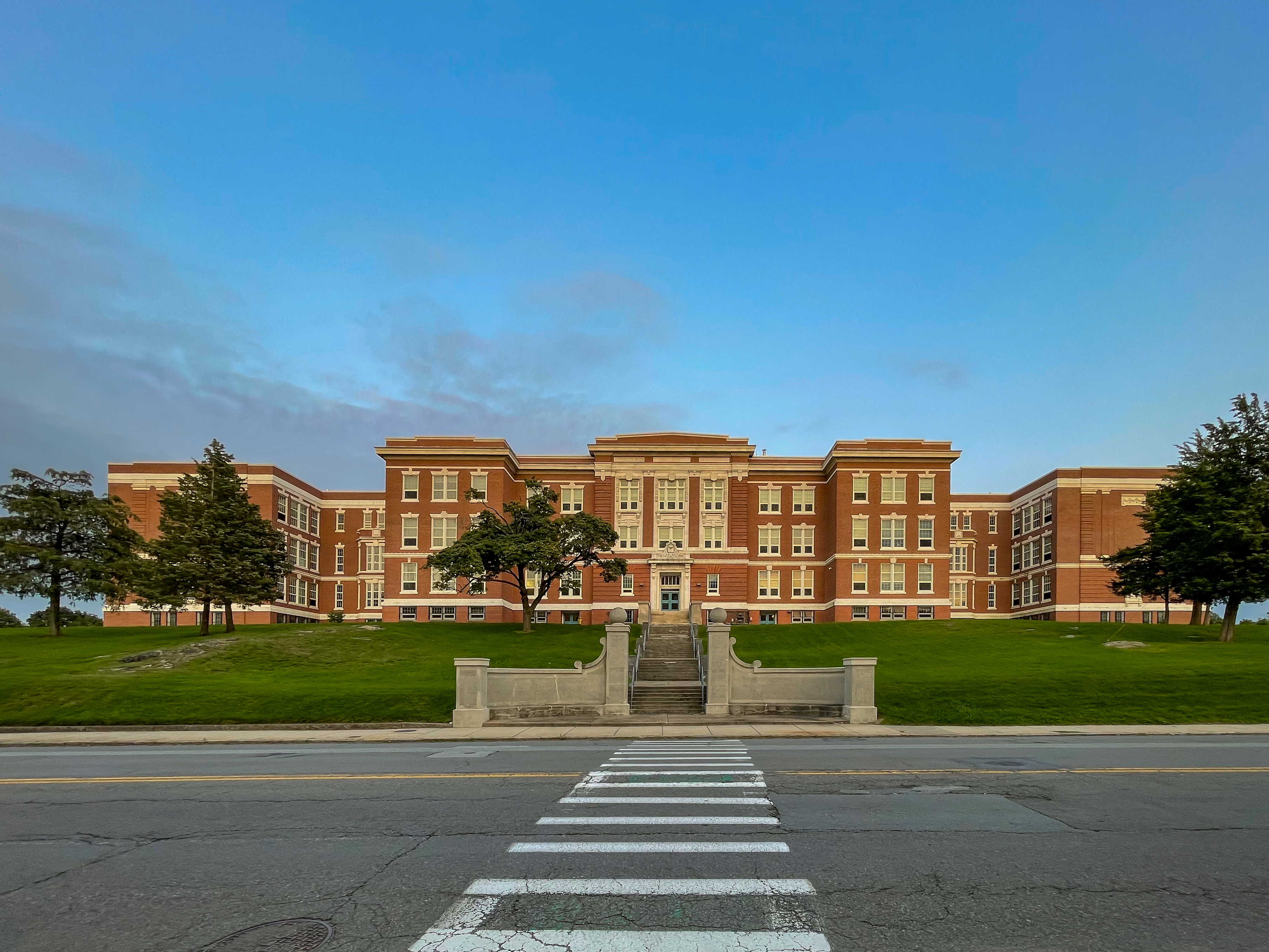 Large red-brick middle school building with symmetrical facade, green lawn, and crosswalk in front.