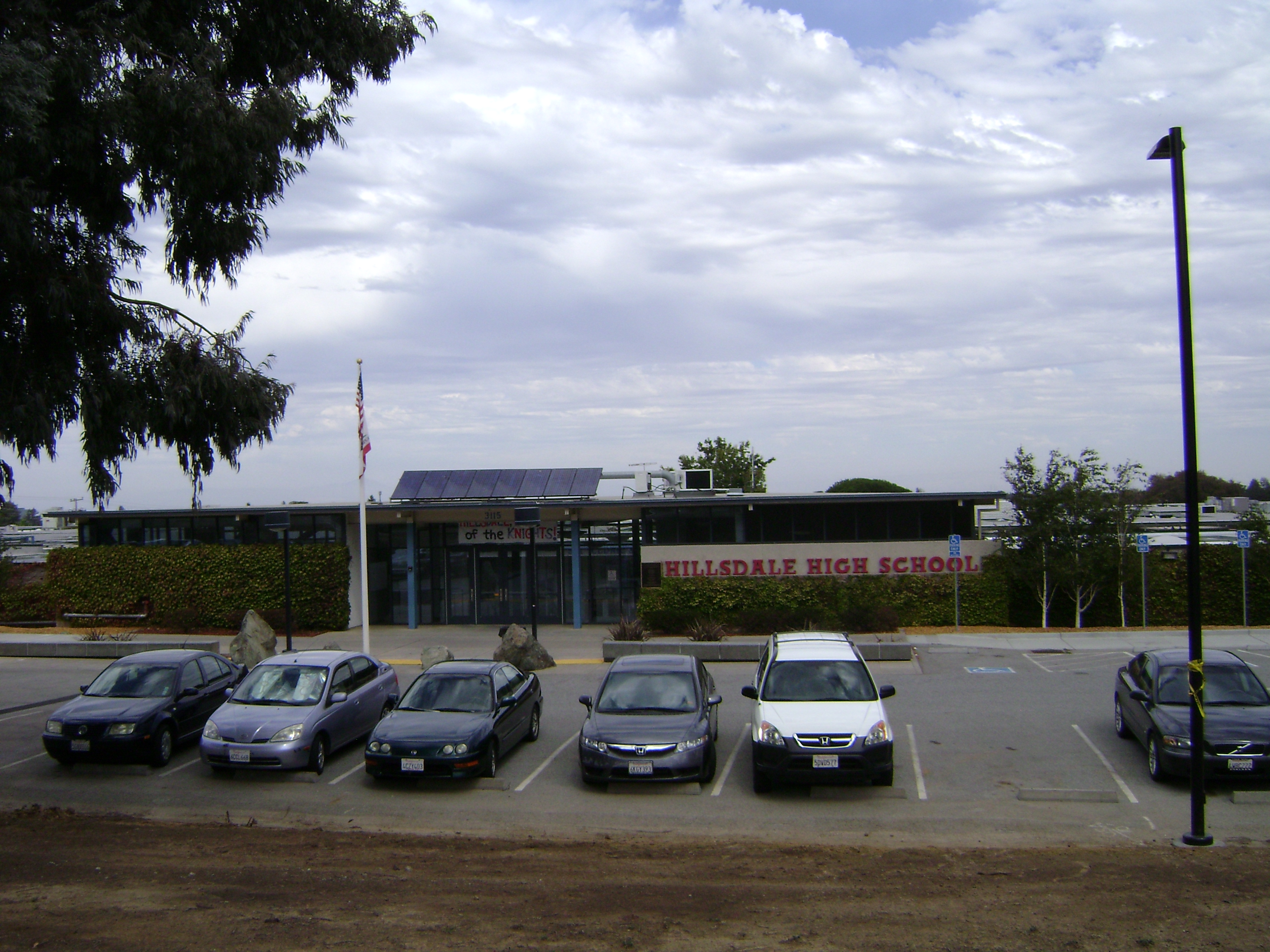 Single-story school building with flagpole and parking lot in front