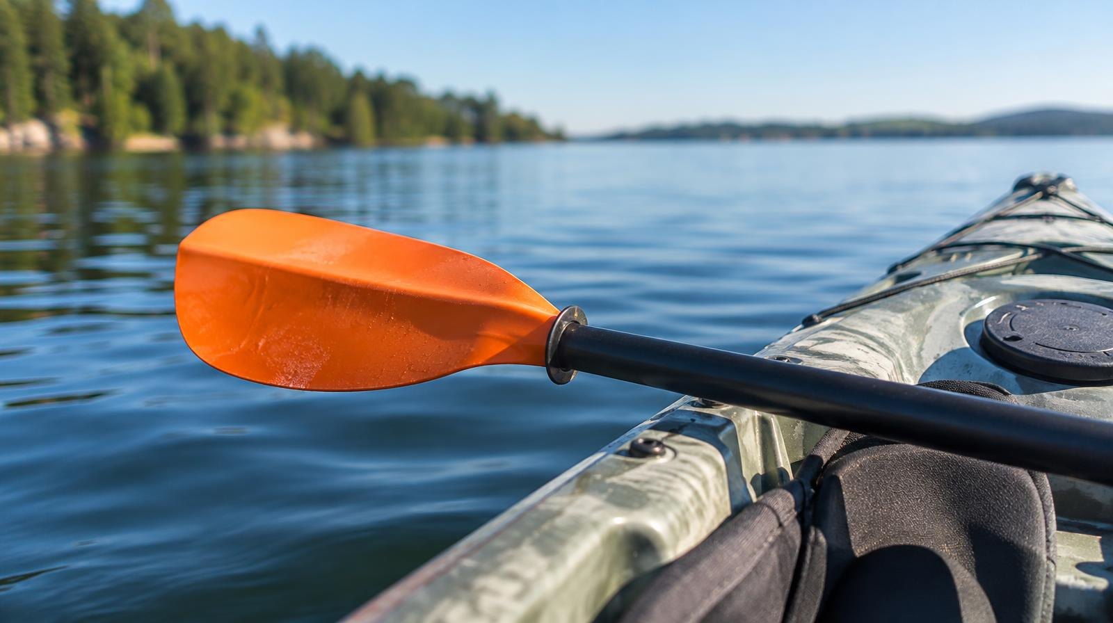 Orange kayak paddle resting across a kayak floating on calm blue water.