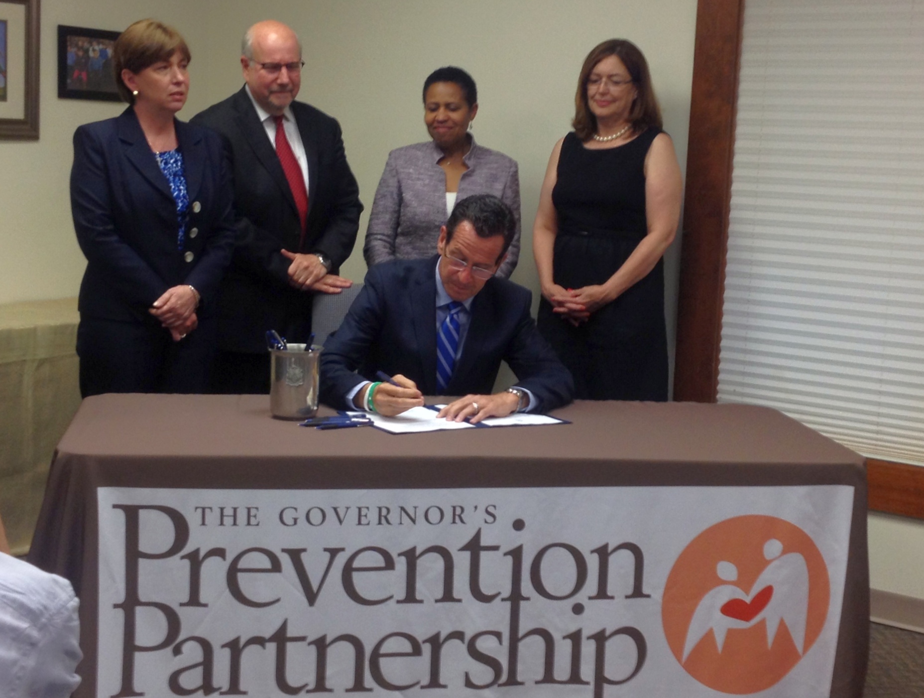 Official signs legislation at a table while four people stand behind him.