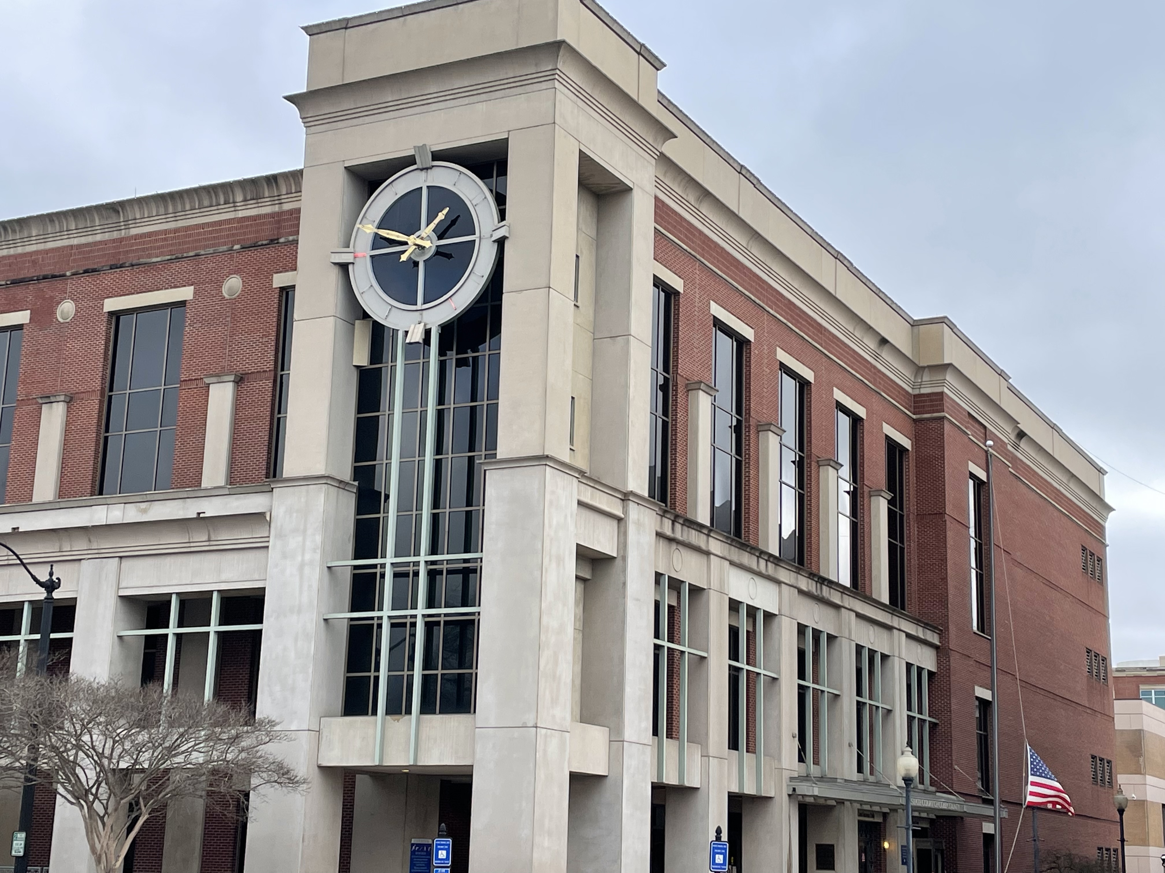 Multi-story brick and stone government building with a large decorative clock and an American flag.