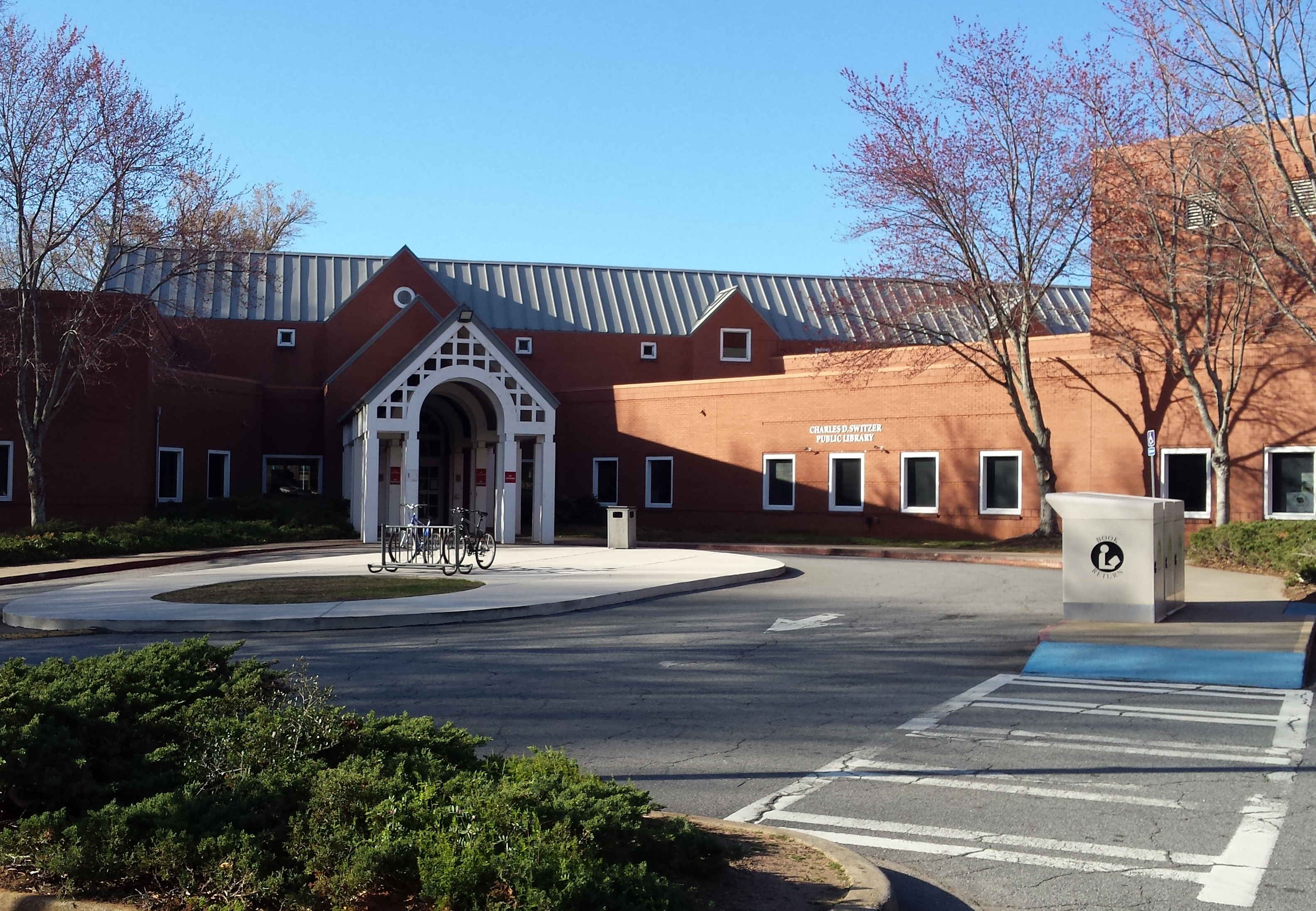 Exterior of a red-brick library building with a white arched entrance and circular driveway.