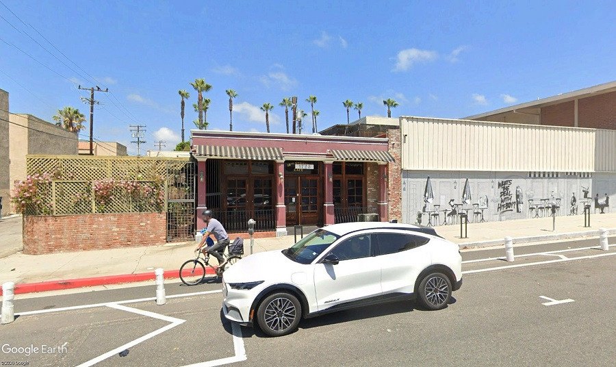 Small brick commercial building with dark striped awning and latticed patio garden.