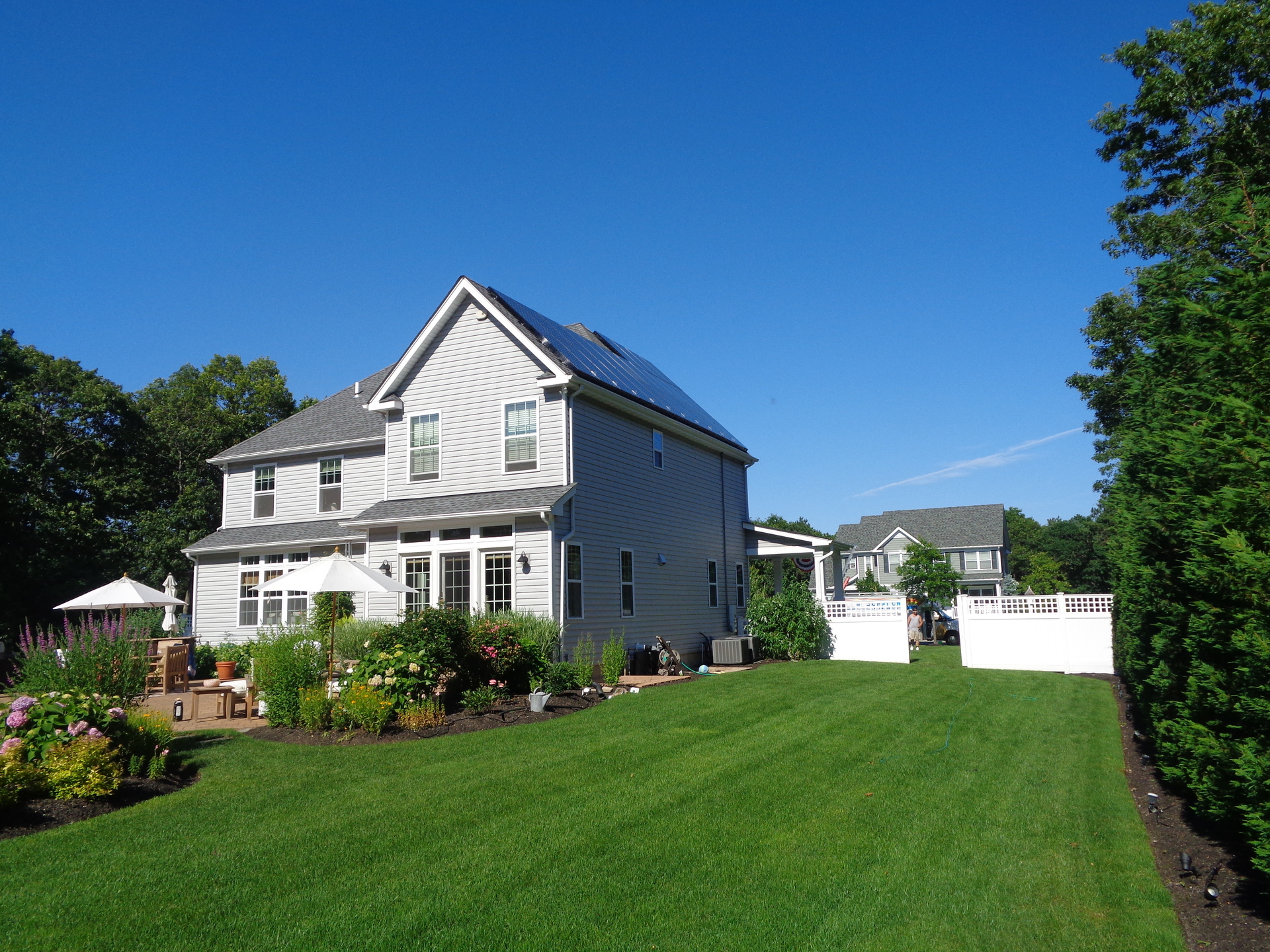 Two-story gray suburban home with solar panels on the roof under a blue sky.