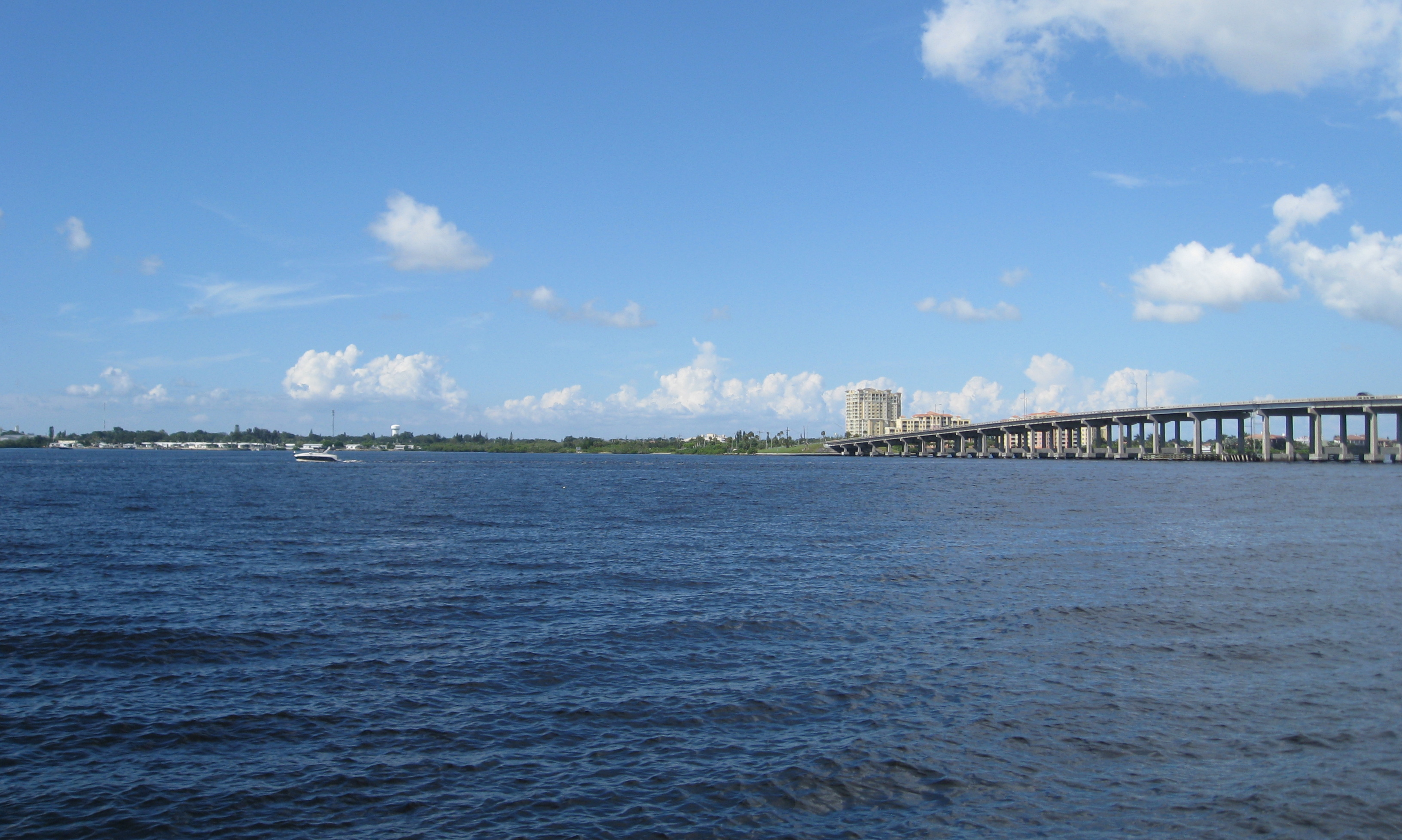 Wide river with a long highway bridge stretching to the far shore under a partly cloudy sky.