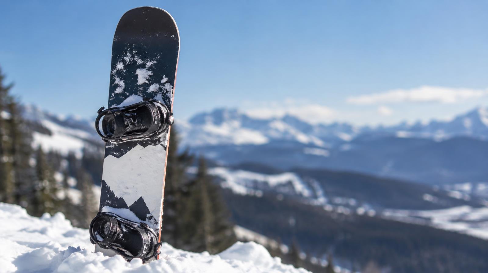 A snowboard standing upright in packed snow on a sunny mountain slope.