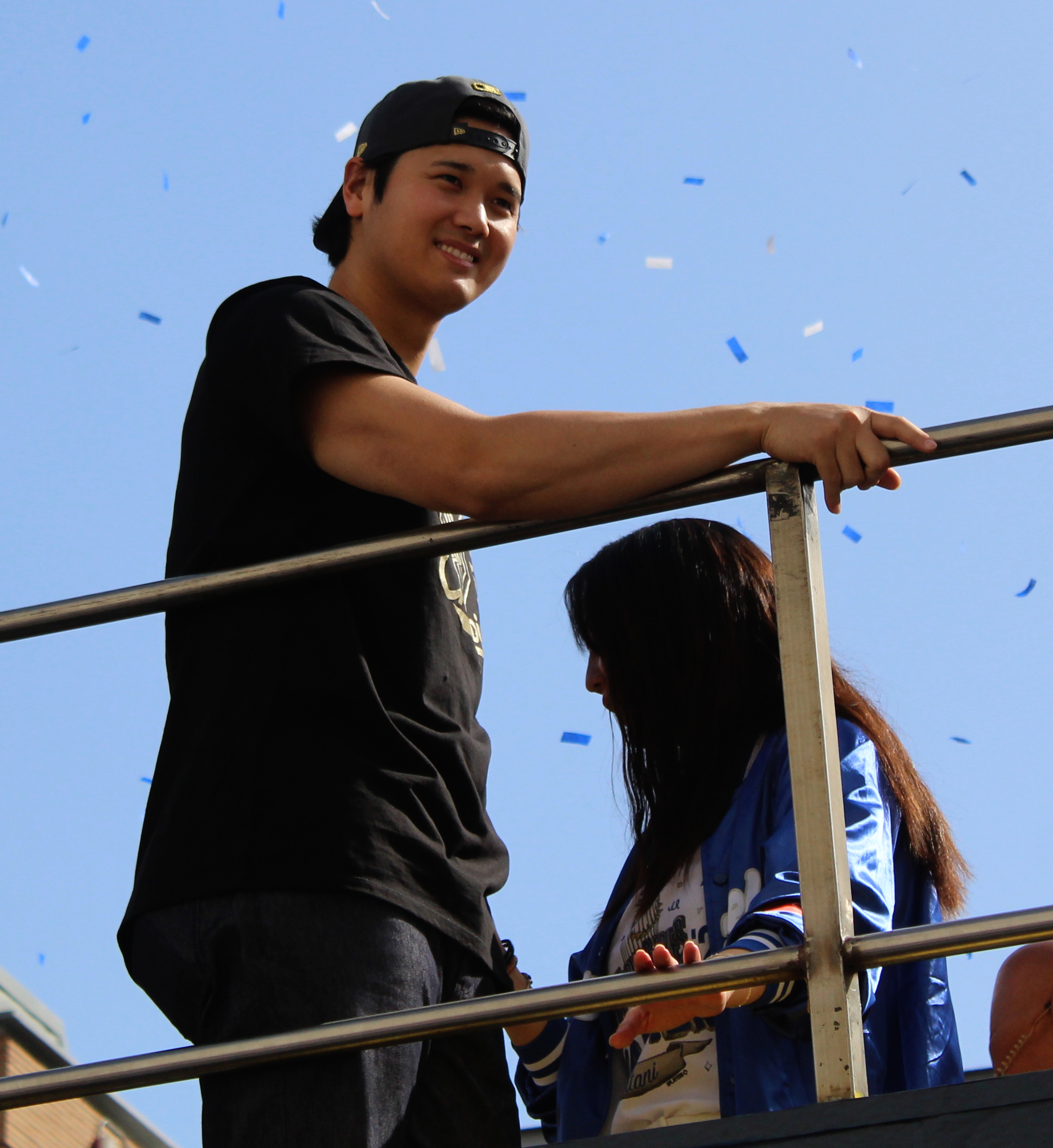 Man in black cap and t-shirt smiling on an elevated float with blue confetti in the air.