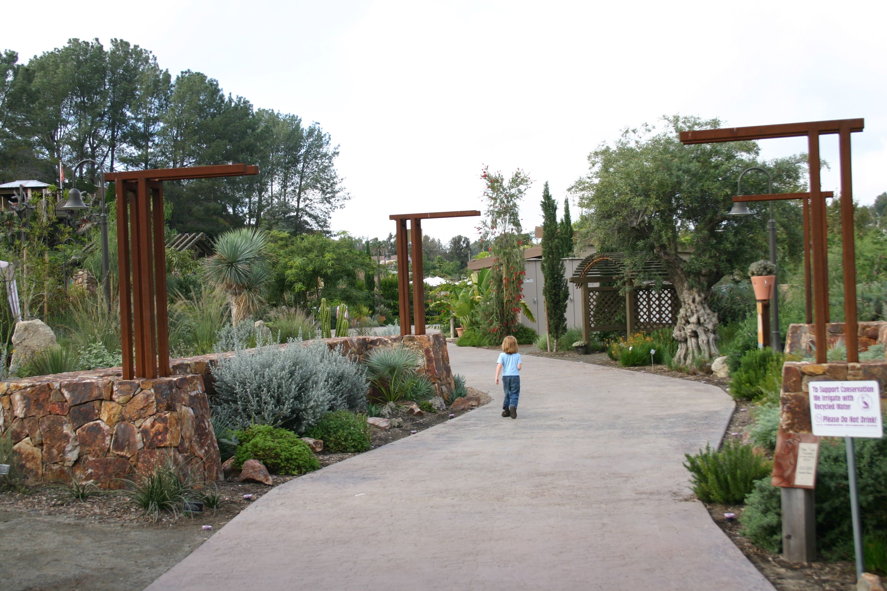 Paved walkway entrance flanked by metal archways and drought-tolerant garden plantings.