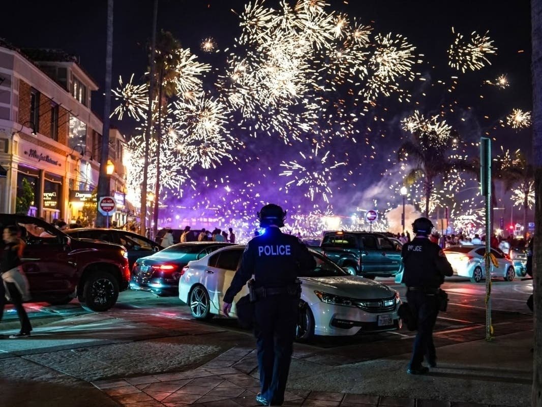 Police officers standing on a commercial street at night with fireworks exploding in the sky above.